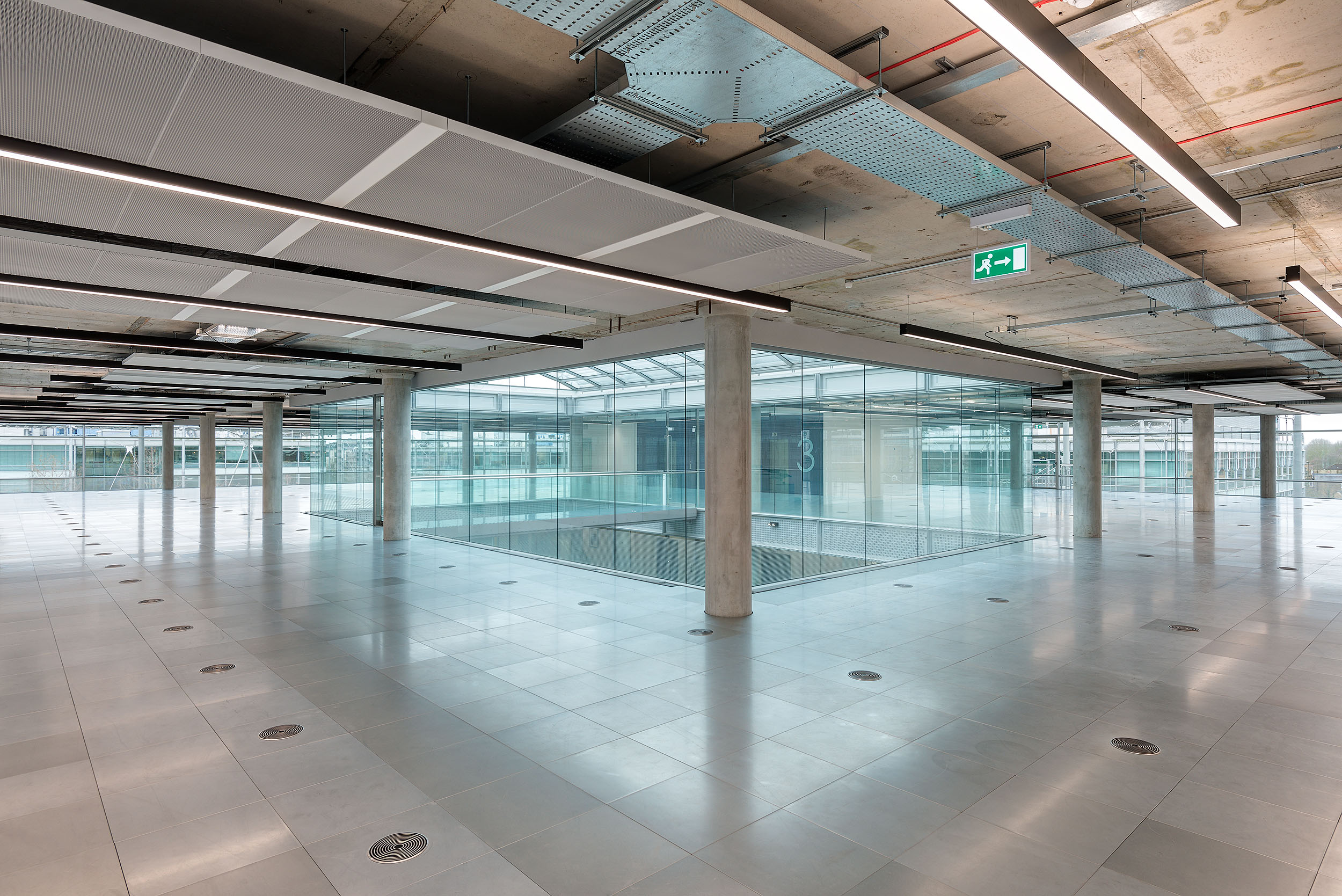 Open workspace at Chiswick Business Park Building 3, showcasing an industrial aesthetic with exposed ceilings, polished flooring, and expansive glass walls, creating a spacious and modern environment.