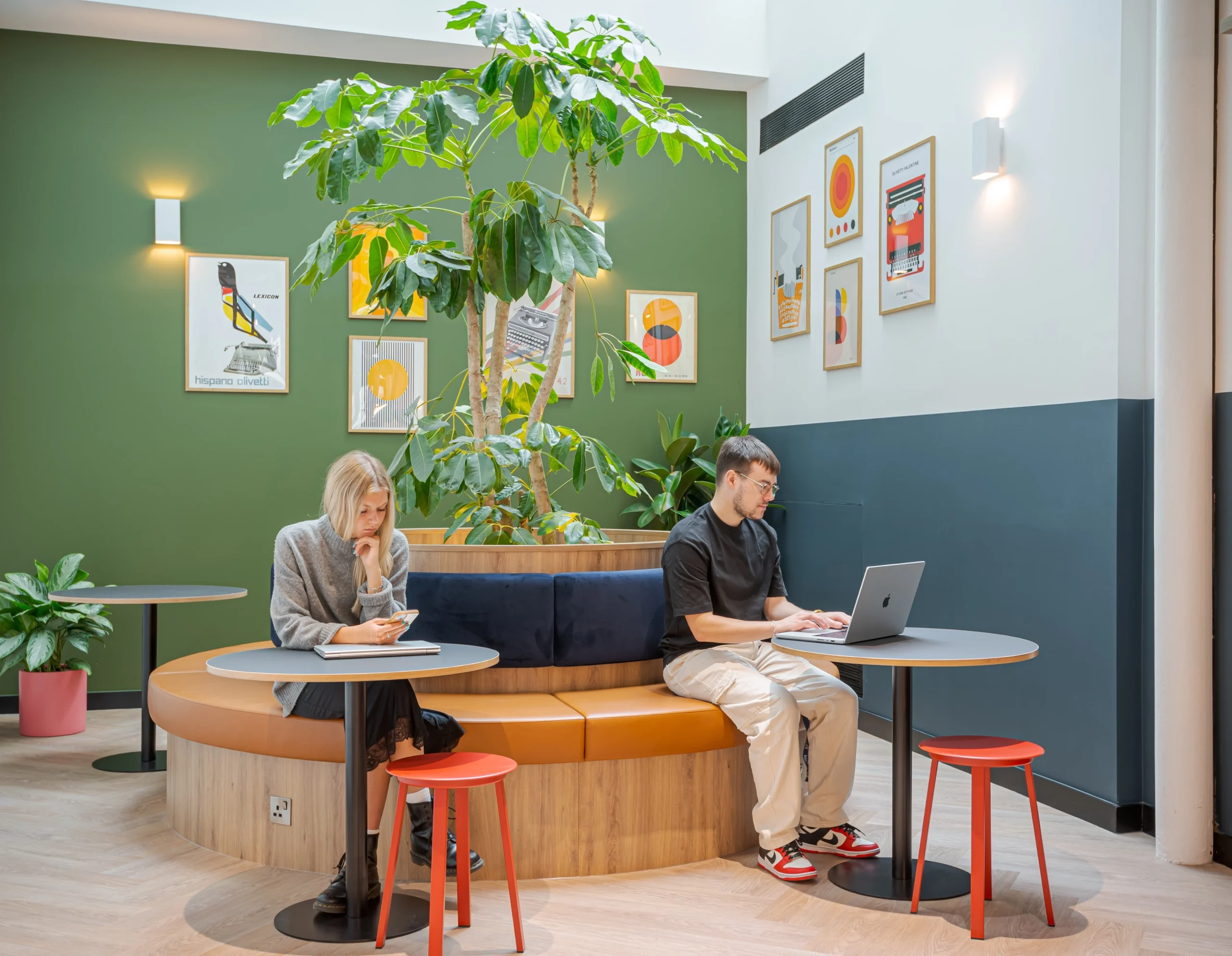 Two employees work at desks surrounded by natural light and greenery