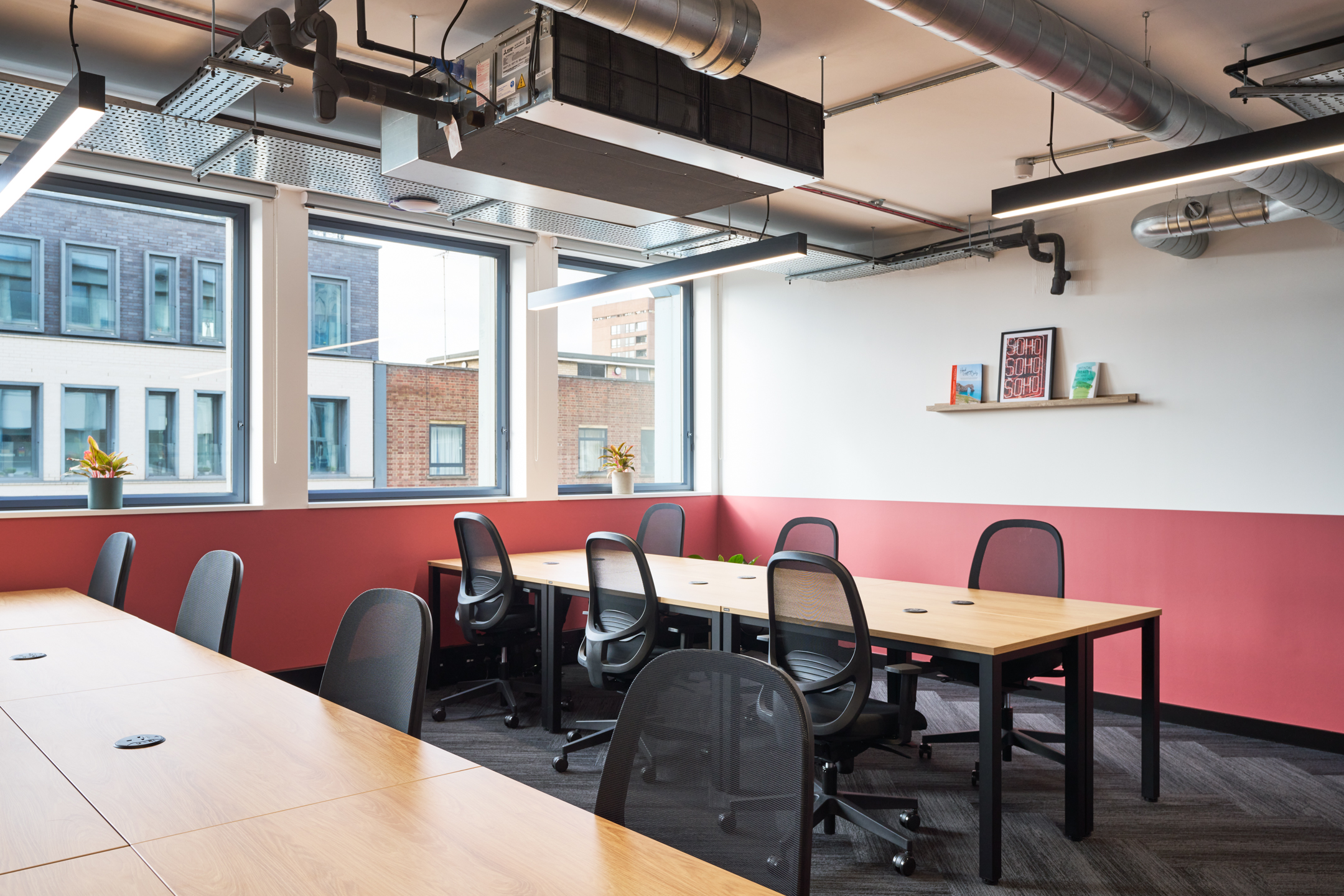 An open workspace at Work.Life's Waverly House, featuring modern desks, ergonomic chairs, vibrant red accents, and large windows offering natural light.