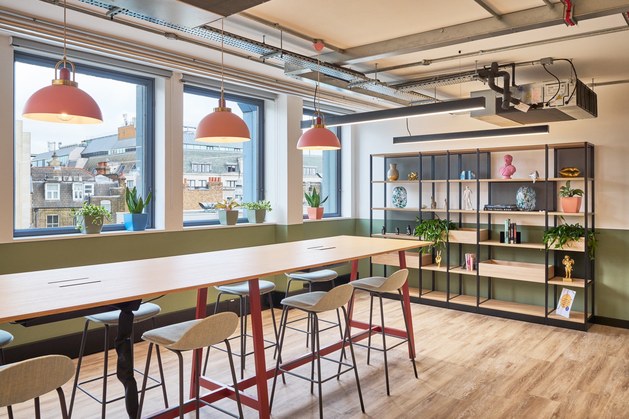 The breakout area at Work.Life's Waverly House, featuring a high table with bar stools, decorative shelving, hanging pendant lights, and large windows with city views.