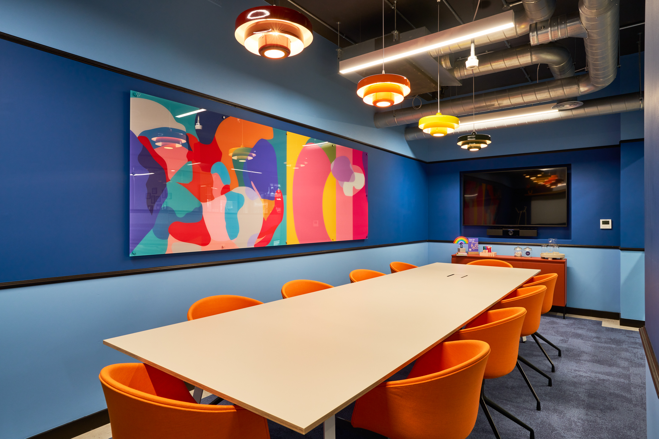 A vibrant meeting room at Work.Life's Waverly House, featuring bold blue walls, colourful artwork, orange chairs, and modern pendant lighting for a dynamic atmosphere.