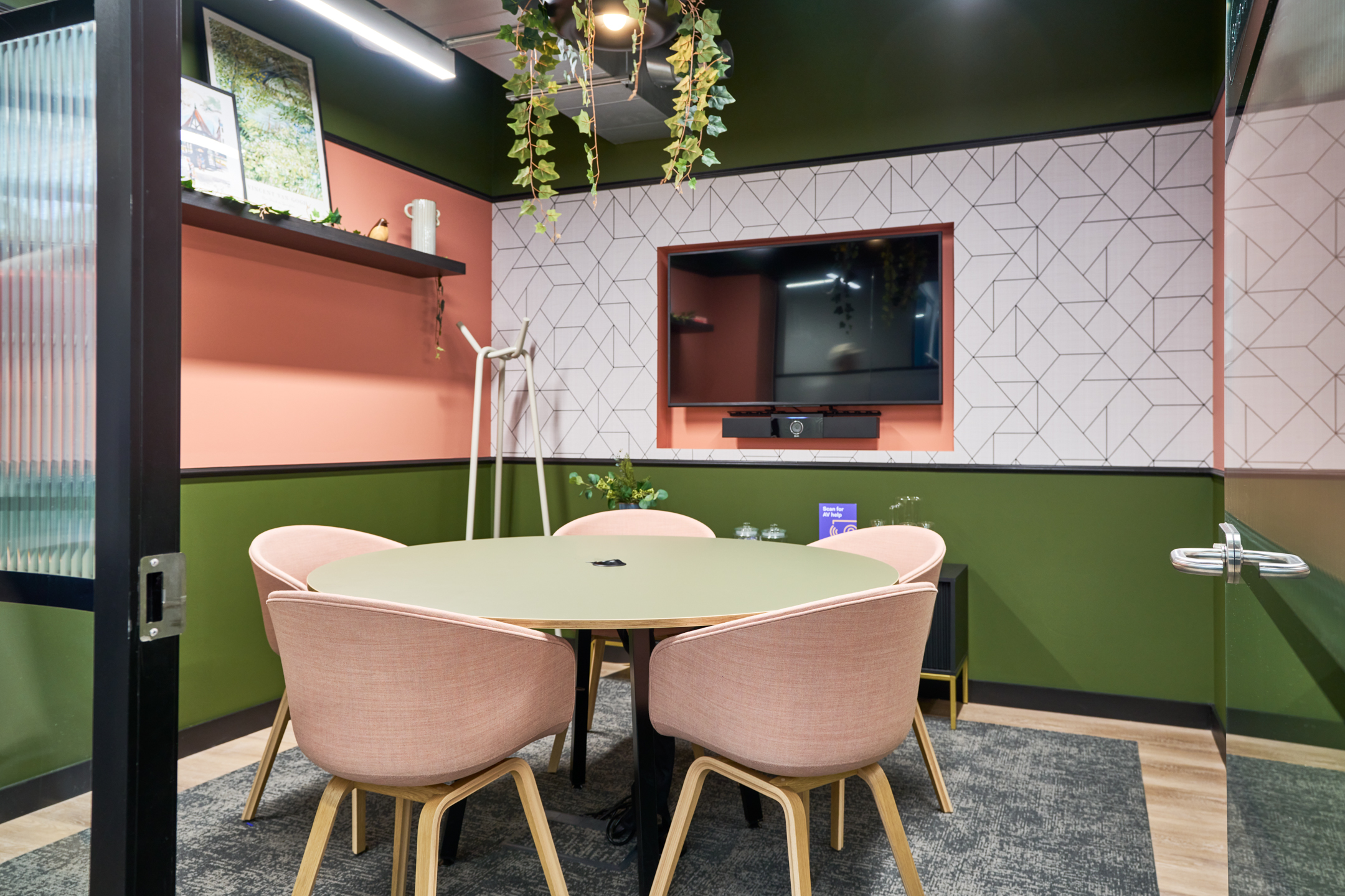 A cosy meeting room at Work.Life's Waverly House, featuring pink chairs, a green table, biophilic accents, and modern geometric wall patterns for a warm atmosphere.