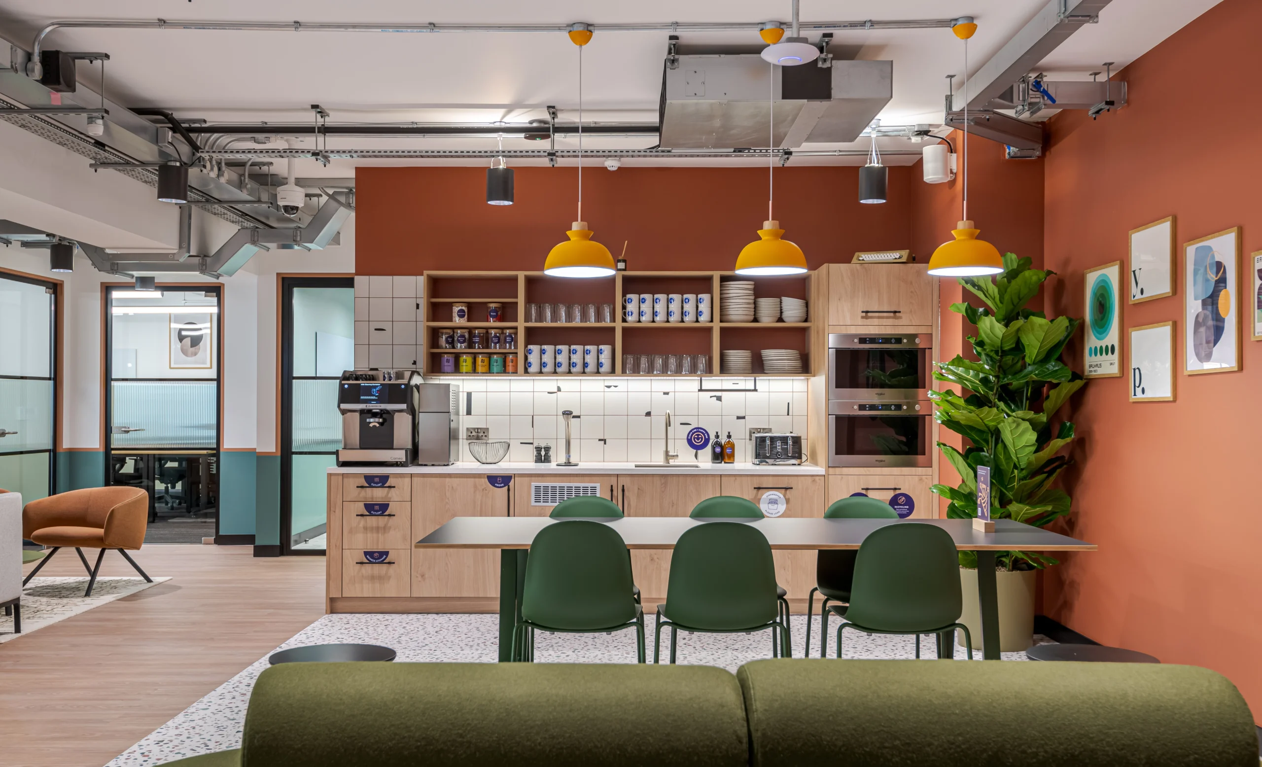 The teapoint at Work.Life’s Typewriter Building, featuring vibrant orange walls, modern cabinetry, a coffee station, and seating with pops of green for a welcoming communal space.