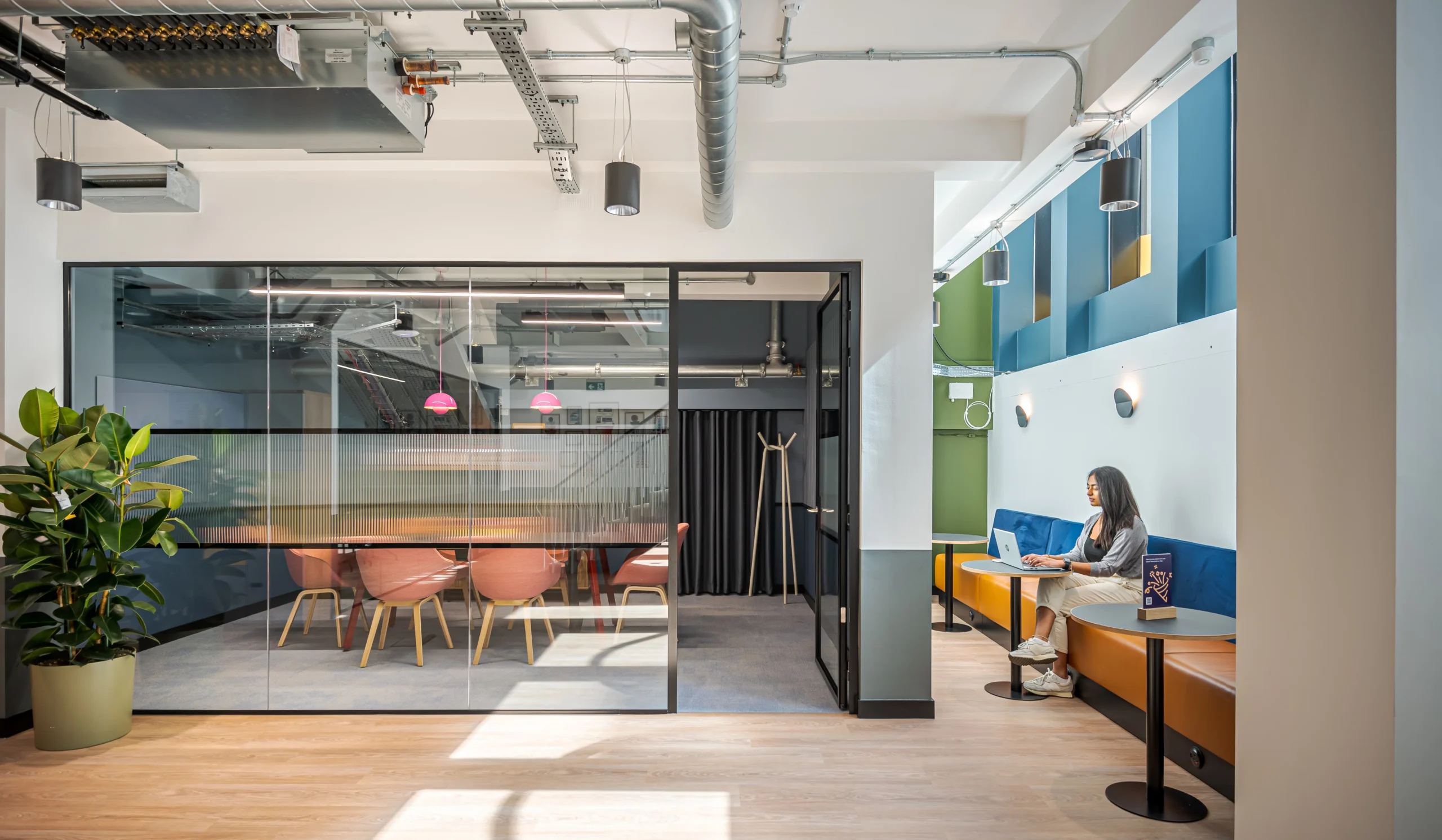 A collaborative space at Work.Life’s Typewriter Building, featuring a glass-enclosed meeting room, vibrant booth seating, natural light, and modern industrial design elements.