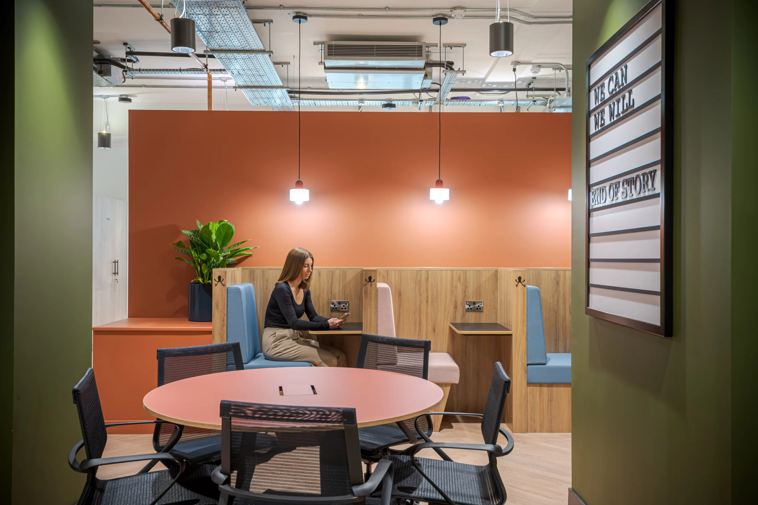 A breakout space at Work.Life’s Typewriter Building, featuring vibrant orange walls, booth seating in pastel tones, pendant lighting, and a motivational wall display.