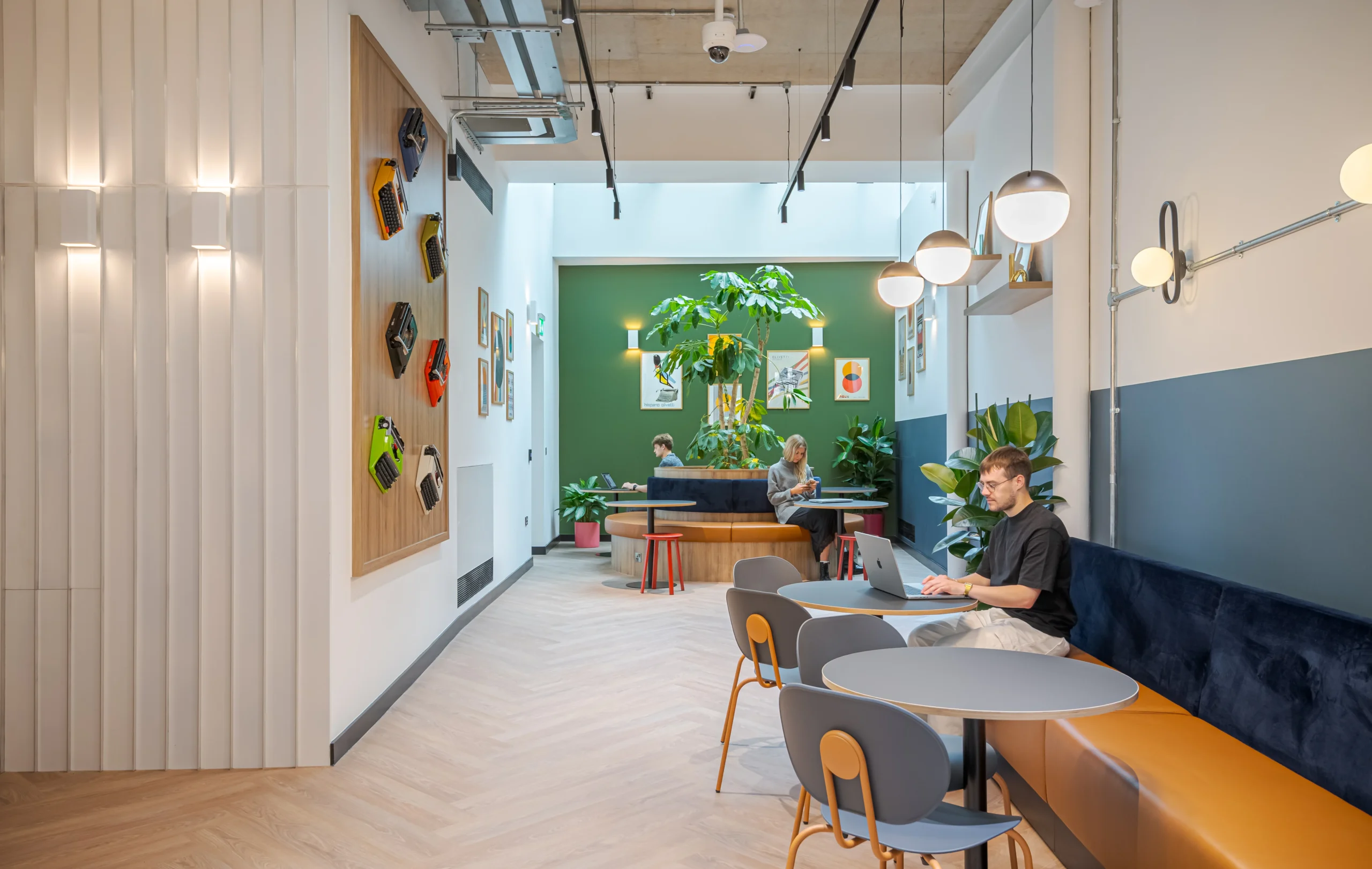 The winter garden at Work.Life’s Typewriter Building, featuring colourful typewriters on display, vibrant seating, lush greenery, and natural light for a biophilic design.