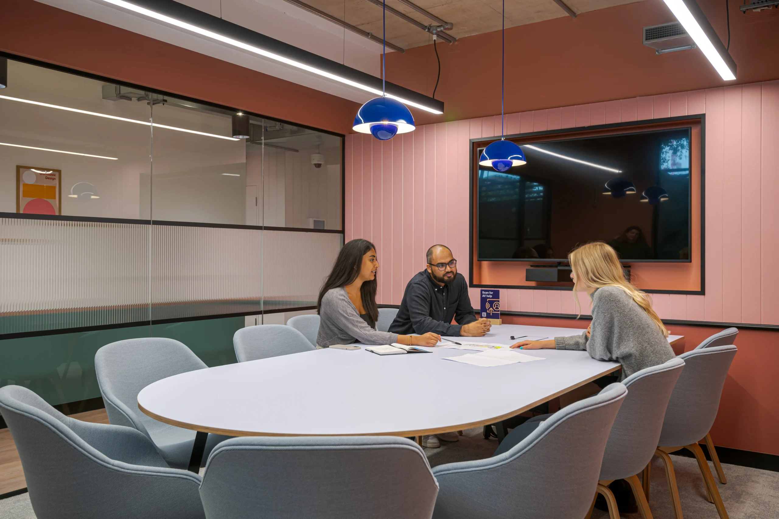 A meeting room at Work.Life’s Typewriter Building, featuring a modern pink and orange design, blue pendant lighting, and a collaborative workspace setup.