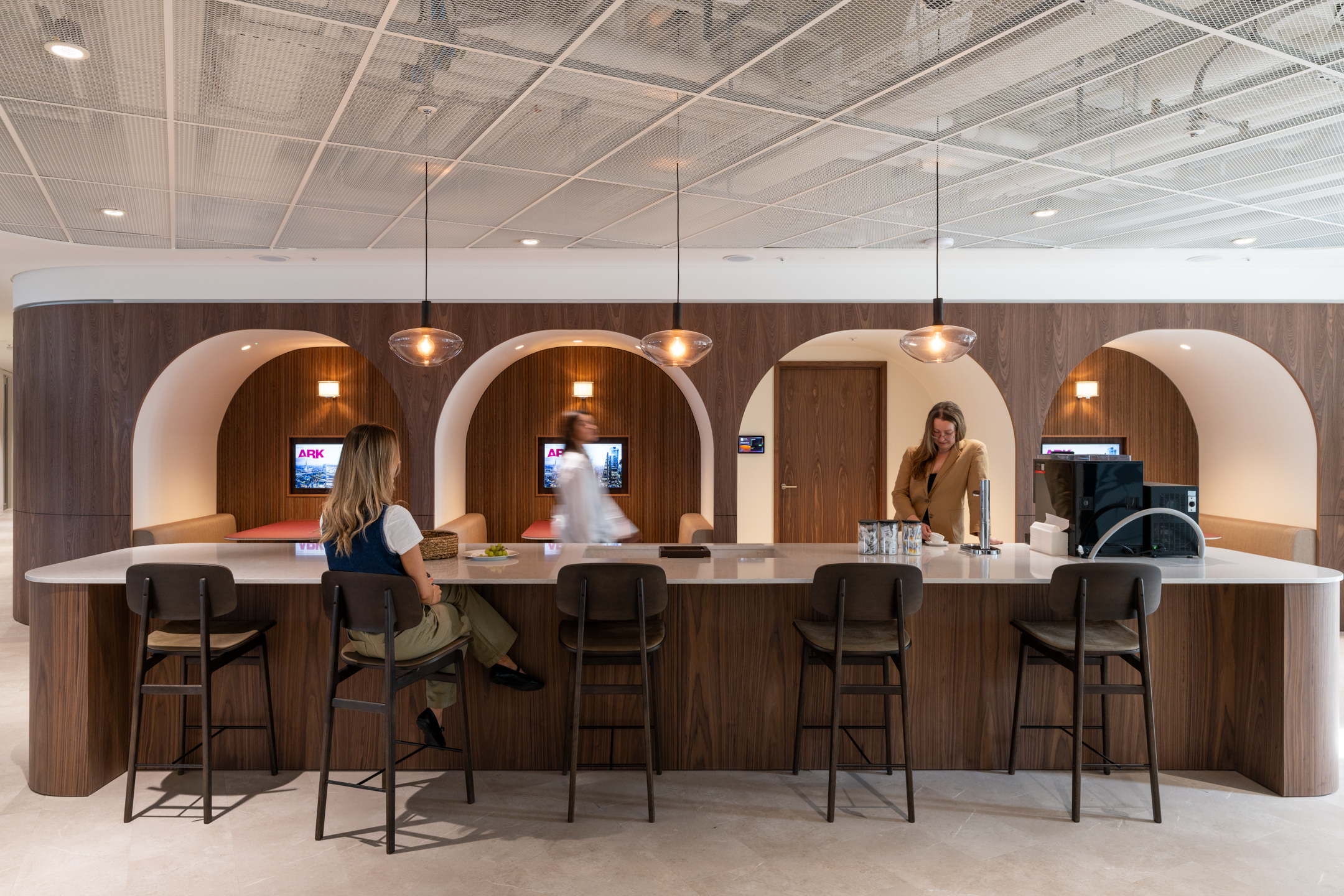 Teapoint counter with integrated seating and arched booths in the Ark Syndicate workspace, featuring warm timber finishes and ambient lighting.