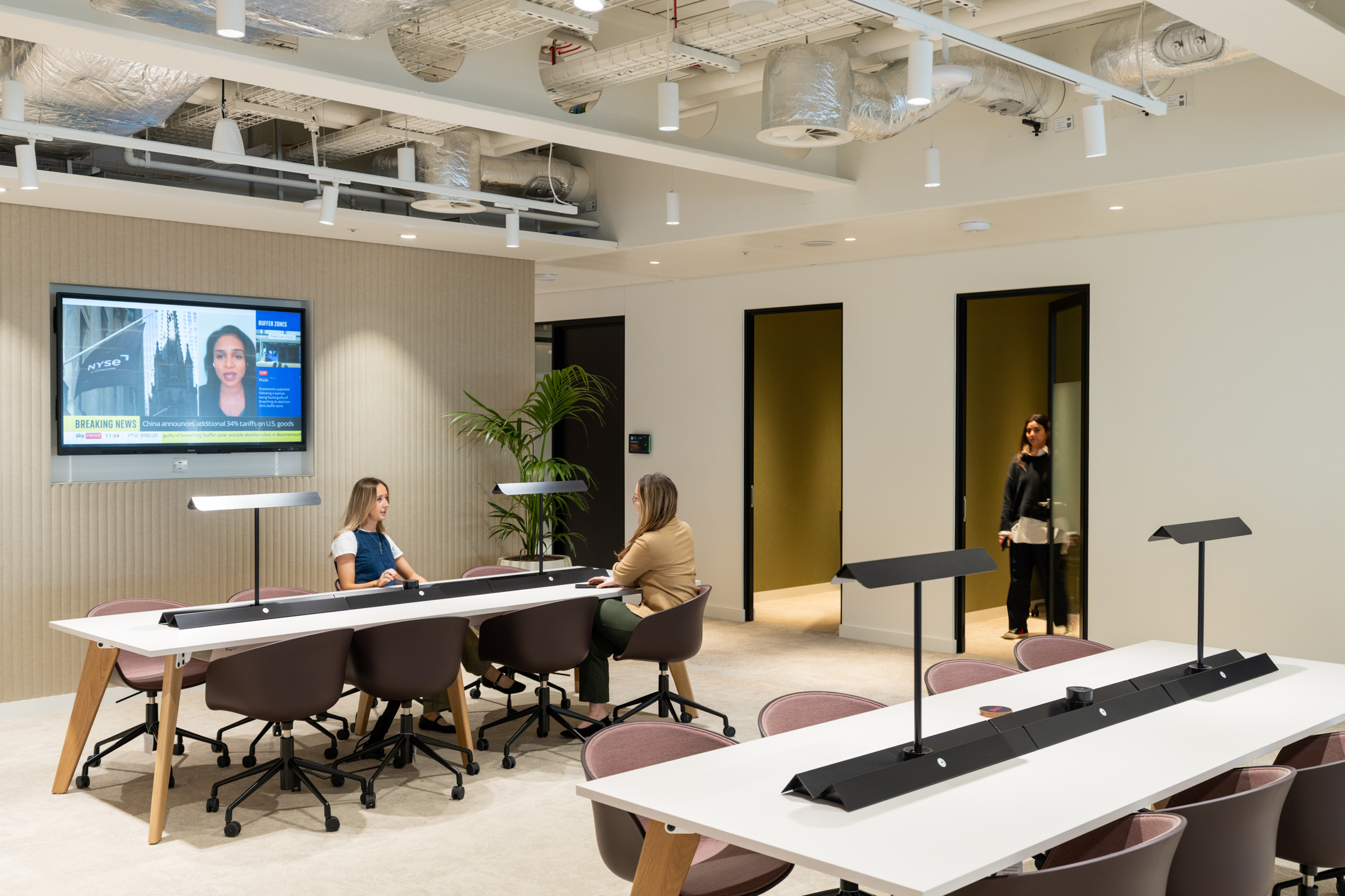 Collaborative workspace in the Ark Syndicate office with modern task lighting, ergonomic seating, and integrated media screen displaying business news.