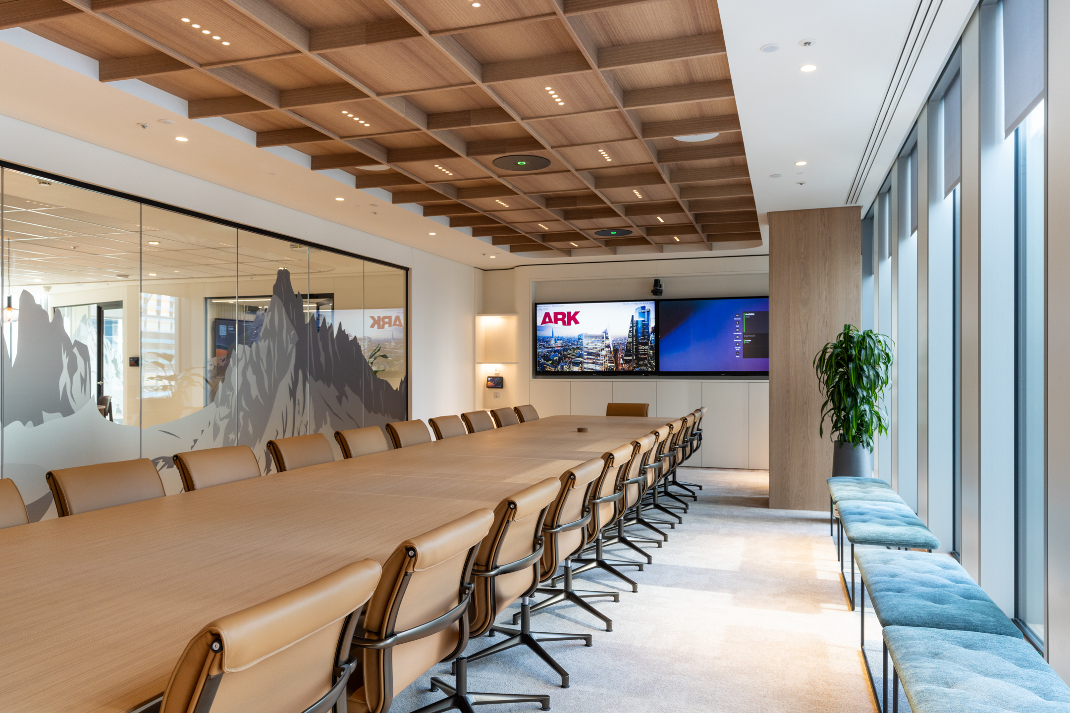 Executive boardroom at Ark Syndicate with a long conference table, leather chairs, coffered timber ceiling, and dual display screens for presentations.