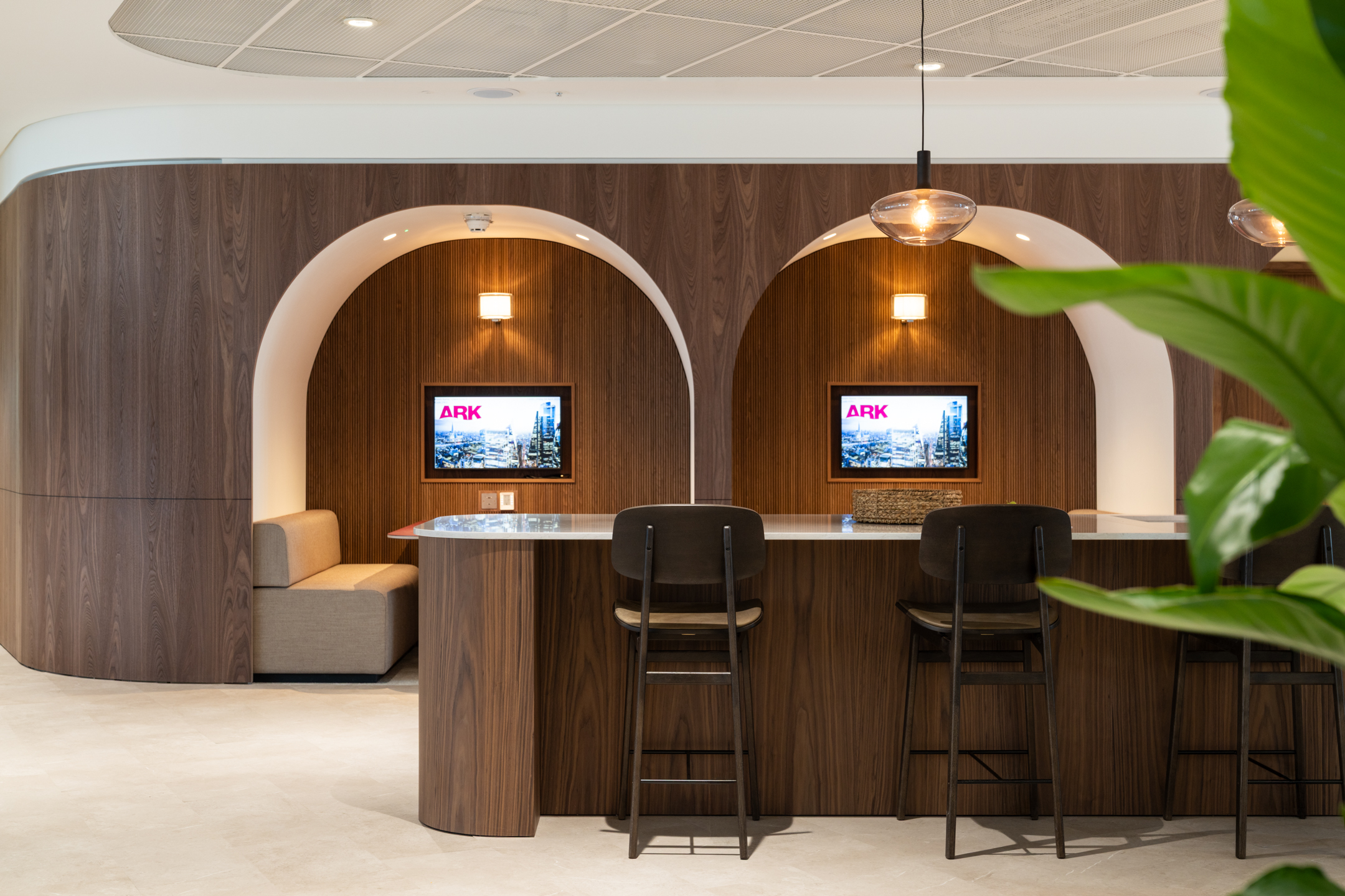 Built-in work booths and high counter seating in the Ark Syndicate office, framed by timber arches with integrated lighting and branded screens.