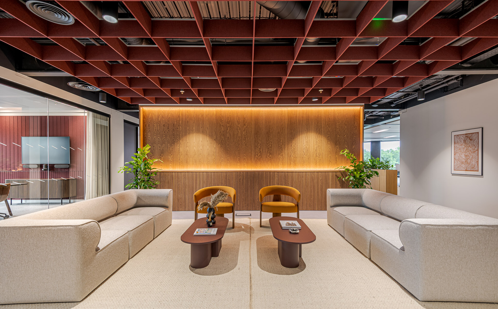 Arbor reception lounge with neutral seating, amber accent chairs and timber-panelled backdrop beneath a red grid ceiling