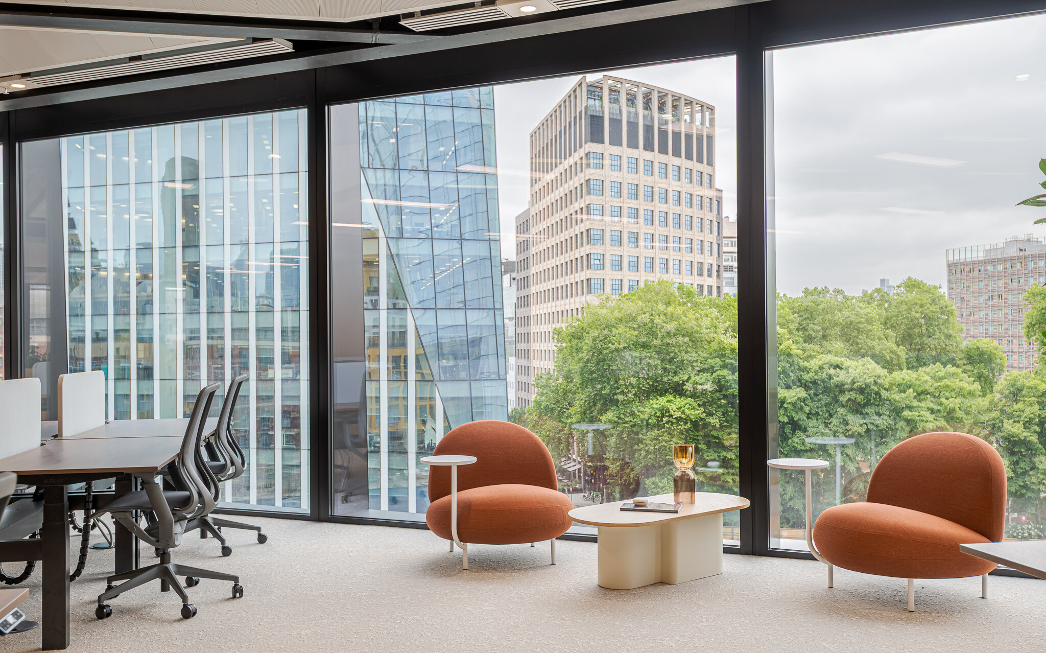 Lounge chairs at Arbor positioned by floor-to-ceiling glazing with views over green spaces and London architecture.