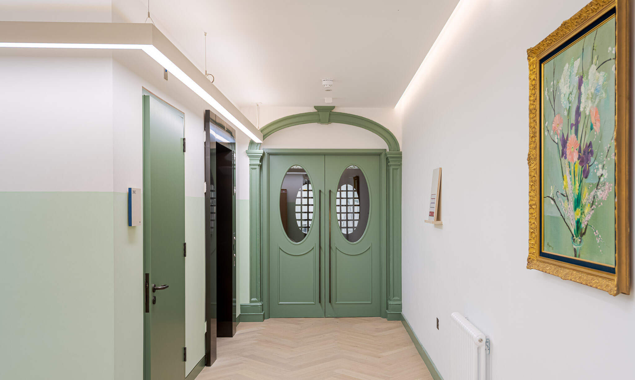 Refined corridor at Bloomsbury House with heritage green double doors, pale timber flooring and pastel wall tones.
