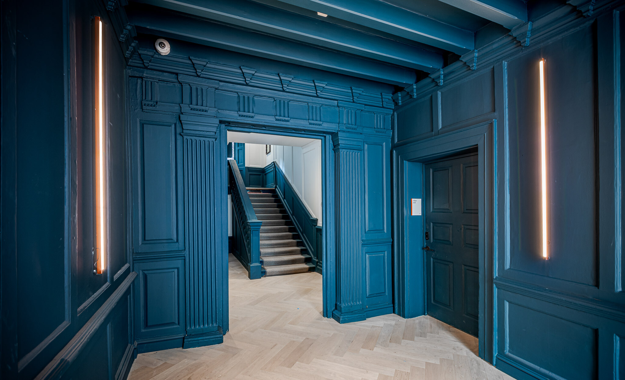 Striking entrance at Bloomsbury House with deep blue panelling, herringbone flooring and modern vertical lighting.