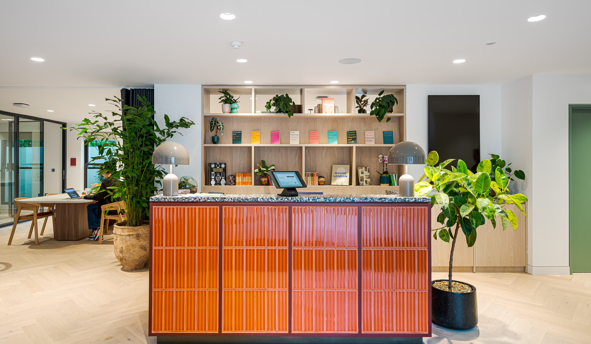 Reception at Bloomsbury House with a glazed orange tiled front, terrazzo counter, and built-in book display.