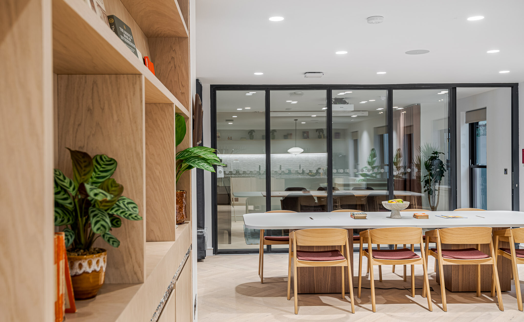 Built-in timber shelving and communal table at Bloomsbury House, with views into the meeting room beyond glass partitions.