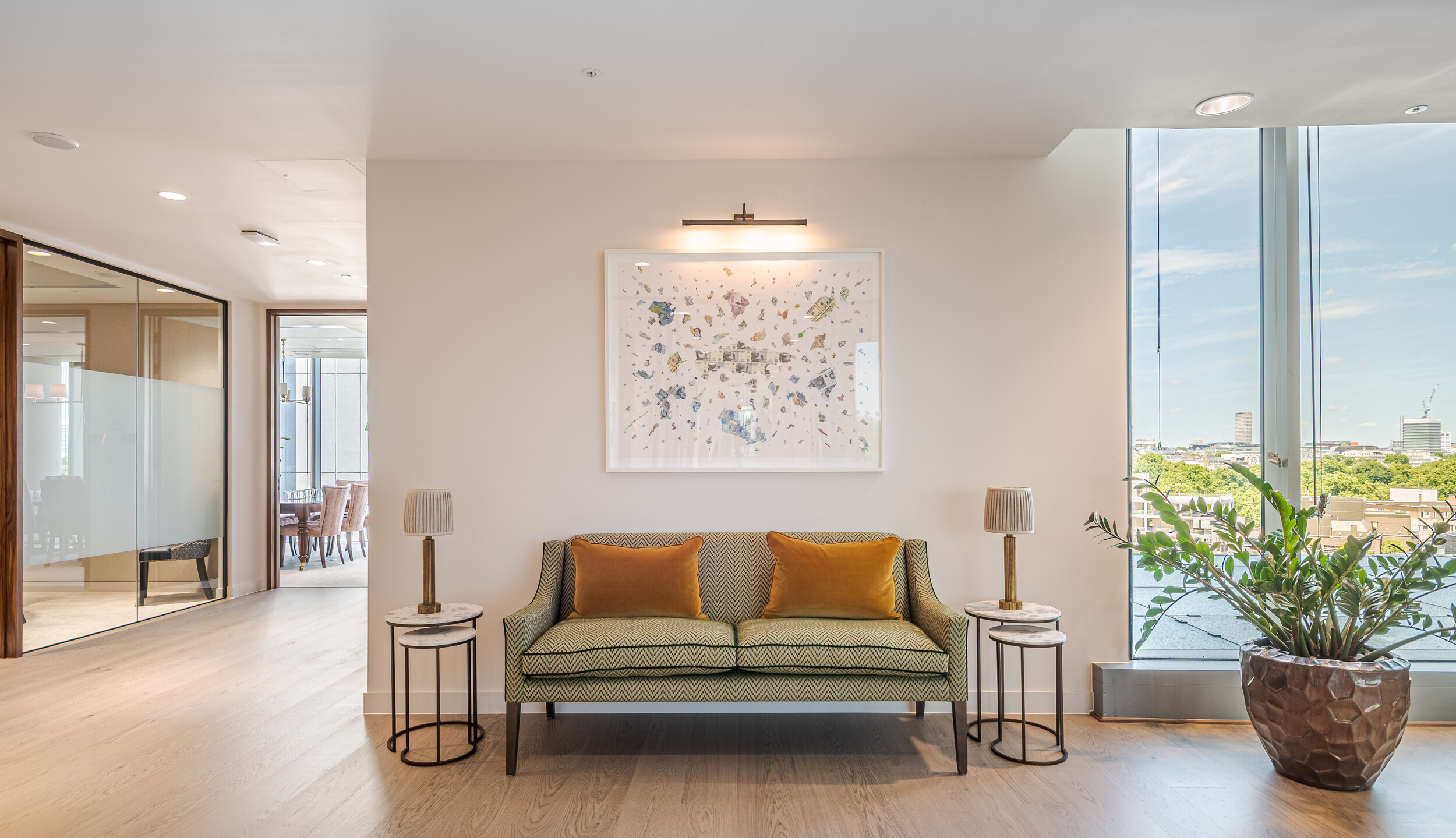 Quiet seating nook in an Investment Management Firm, featuring a patterned two-seater sofa with ochre cushions and framed abstract artwork. Twin marble side tables and floor-to-ceiling glazing bring sophistication and light into the space. A sculptural planter adds a refined biophilic element.