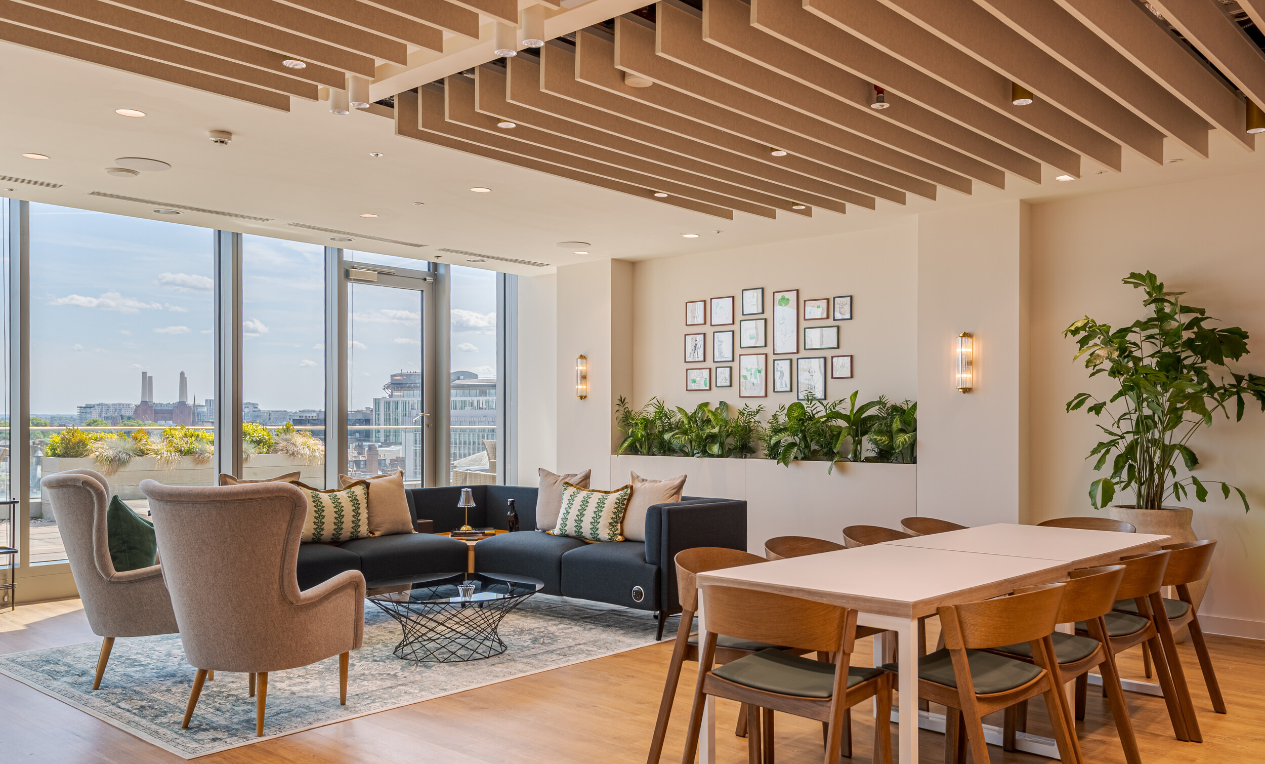 Breakout space in an Investment Management Firm, combining lounge and dining areas with sweeping views of London. Acoustic ceiling baffles and integrated planters create a calm, comfortable environment. A gallery wall and mix of soft seating add a curated, homely feel.