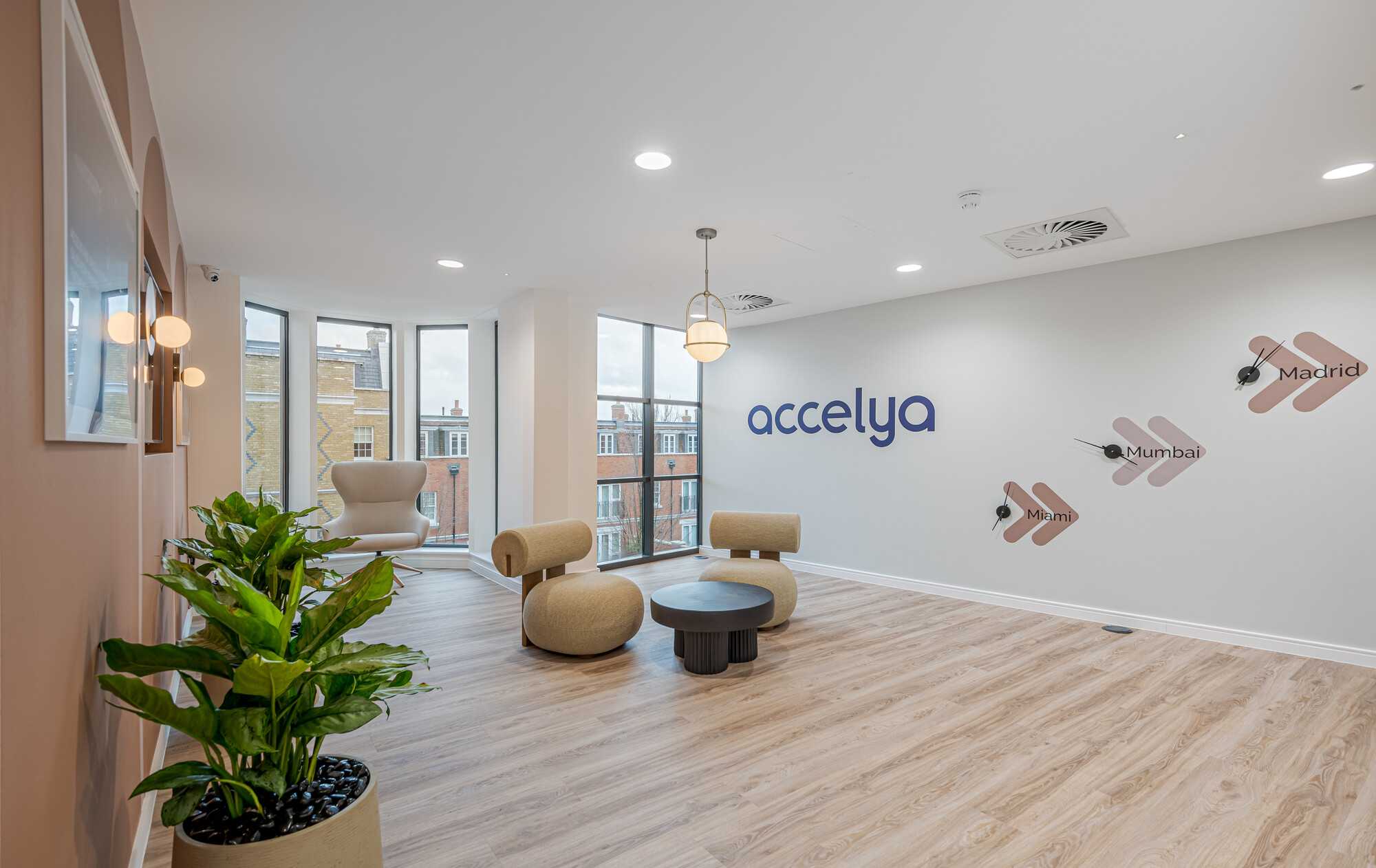 Accelya office designed by Two, featuring a lounge area with beige chairs, a black round table, and a light fixture.