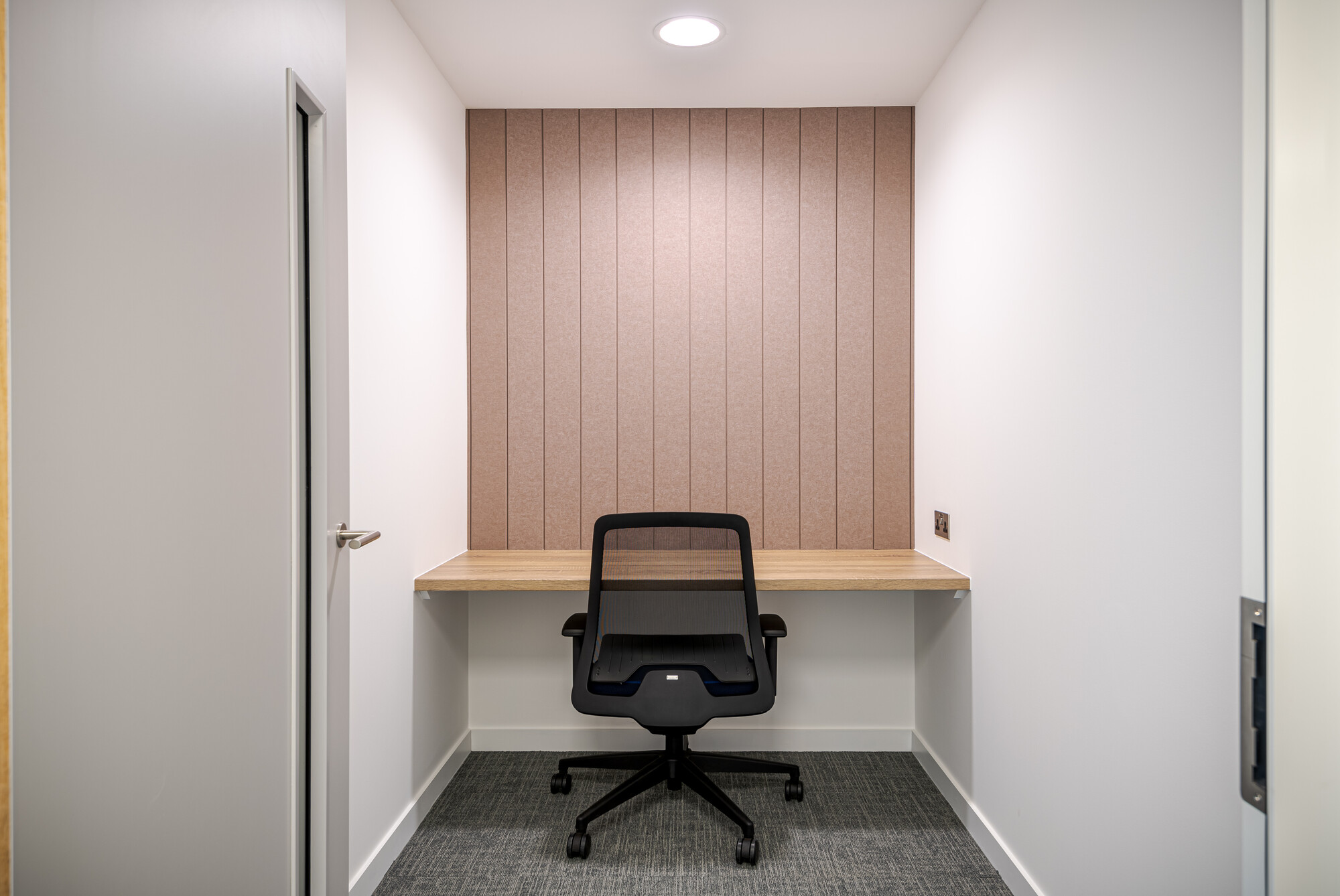 Privacy room in Accelya's office by Two, designed for individual use. The space includes a built-in wooden desk, a black mesh office chair, and a textured wall panel in a neutral tone.