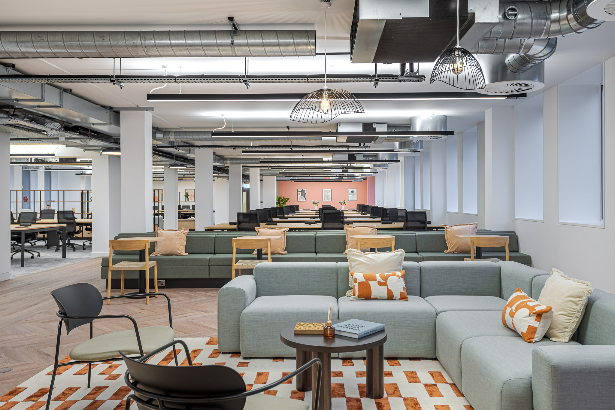 Open-plan workspace designed for an Asset Management Firm, featuring soft seating, exposed services, and flexible desking zones with a balance of industrial finishes and warm textures.