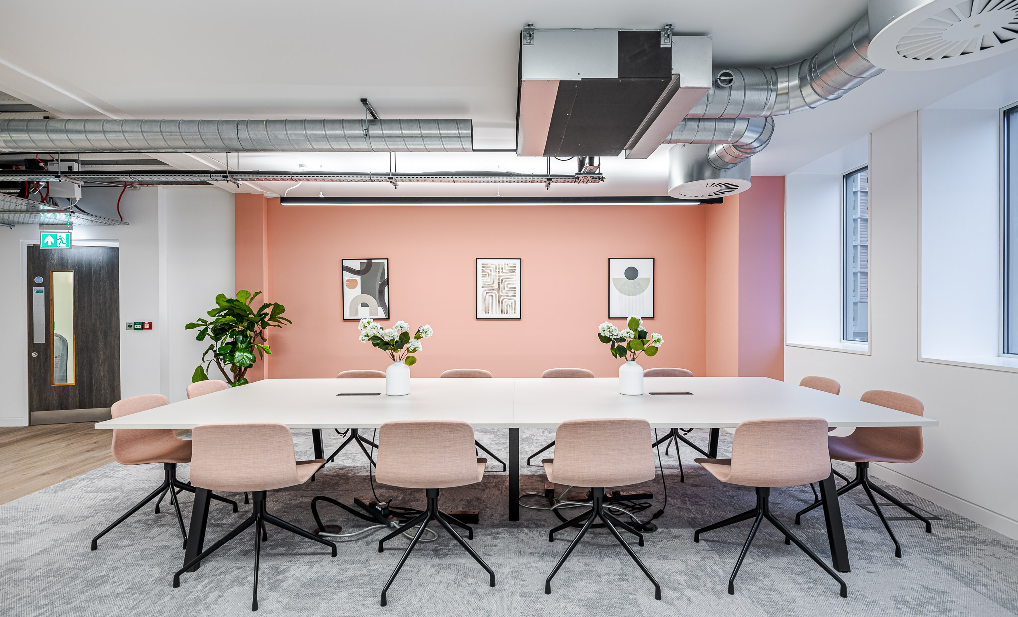 Contemporary meeting room in an Asset Management Firm office, featuring blush-toned chairs, a white conference table, and a coral accent wall with modern artwork and natural light.