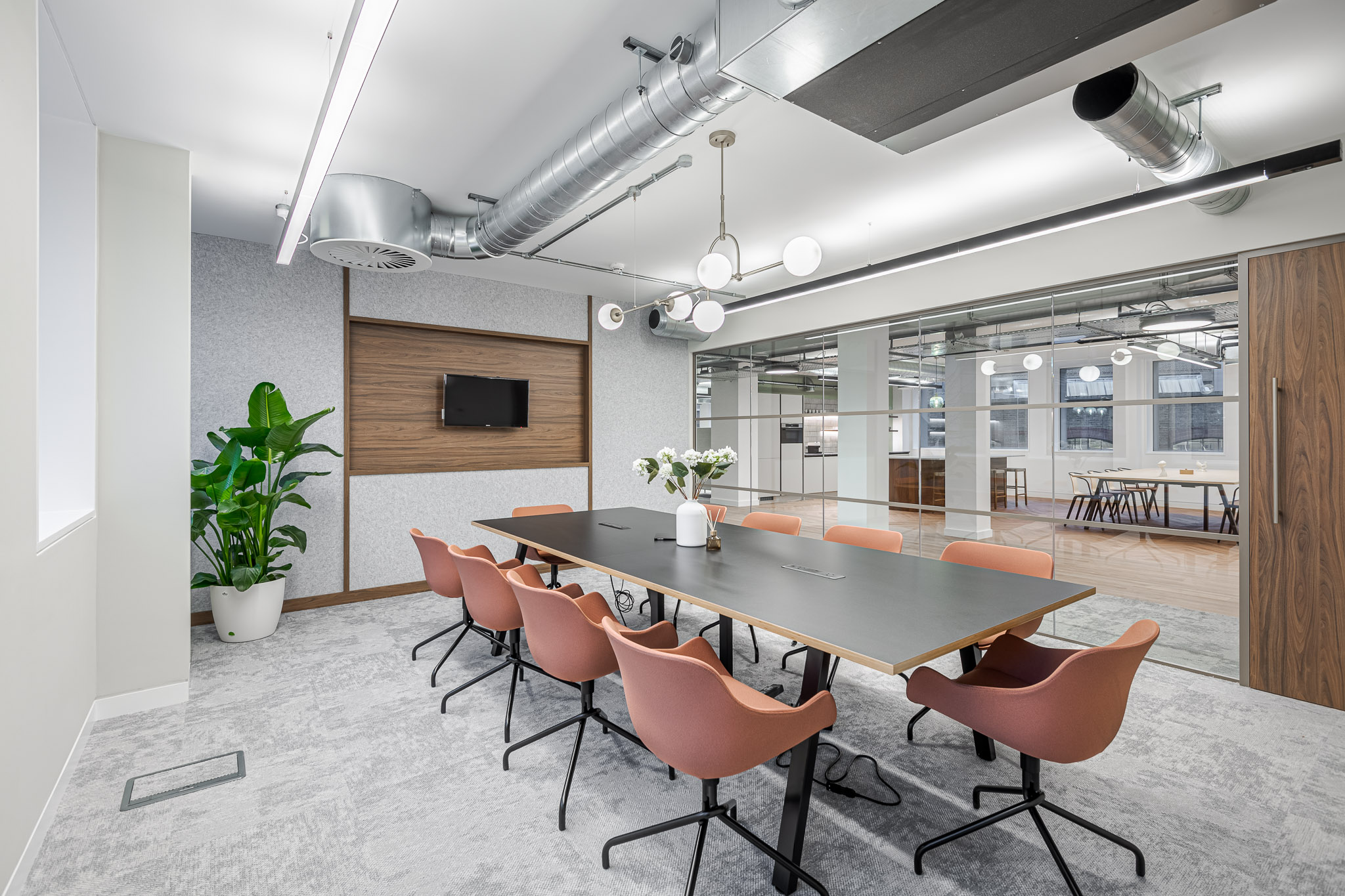 Glass-fronted meeting room in an Asset Management Firm Tenant-Ready™ space, styled with rust-toned chairs, a matte black table, and warm wood accents for a contemporary professional feel.