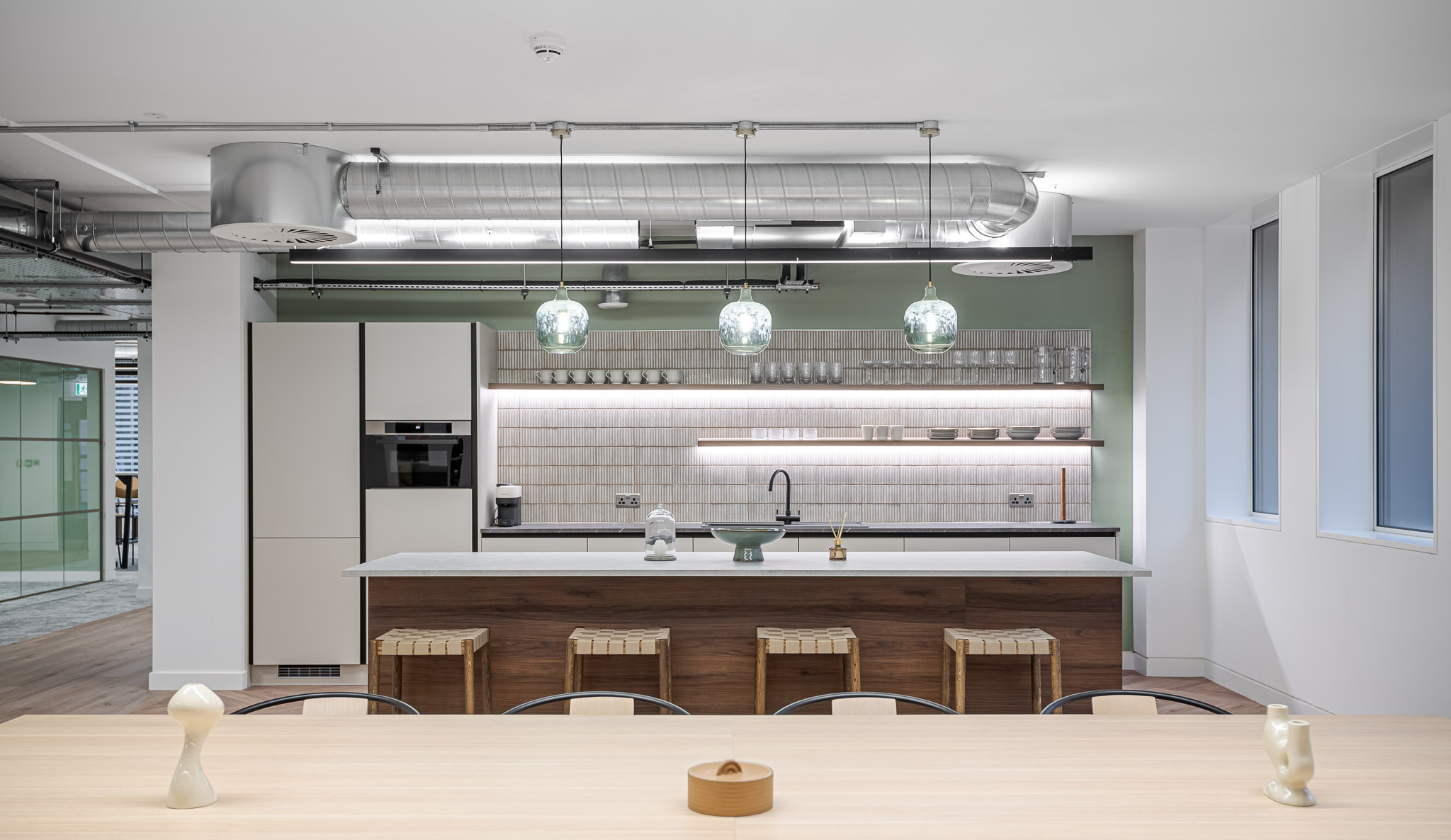 Teapoint area in the Asset Management Company Tenant-Ready™ space, featuring a green-tiled splashback, open shelving, pendant lighting, and a central island with wood-fronted stools.