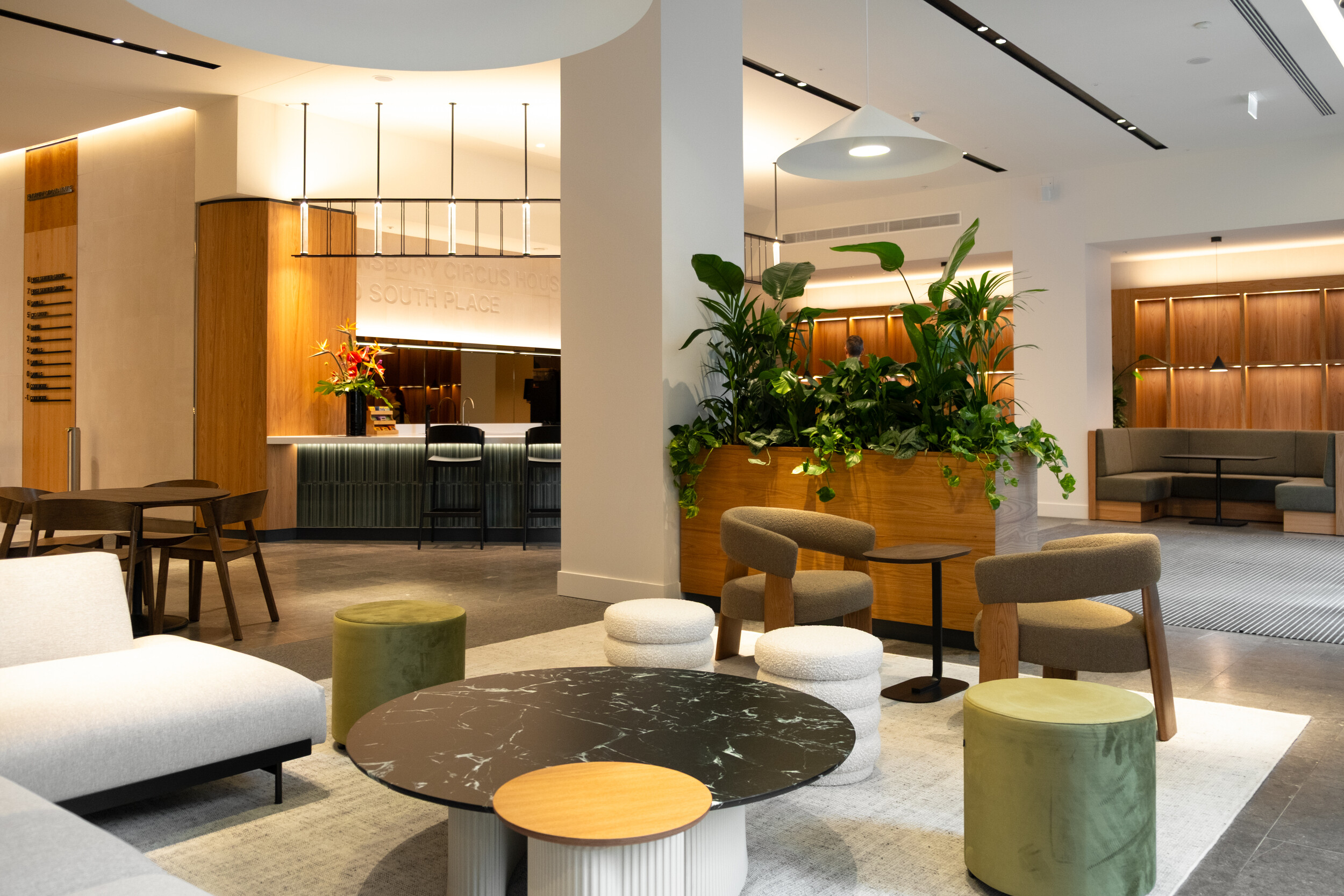 Modern reception area at Finsbury Circus House with contemporary seating, marble-topped coffee tables, wood accents, and lush indoor plants.