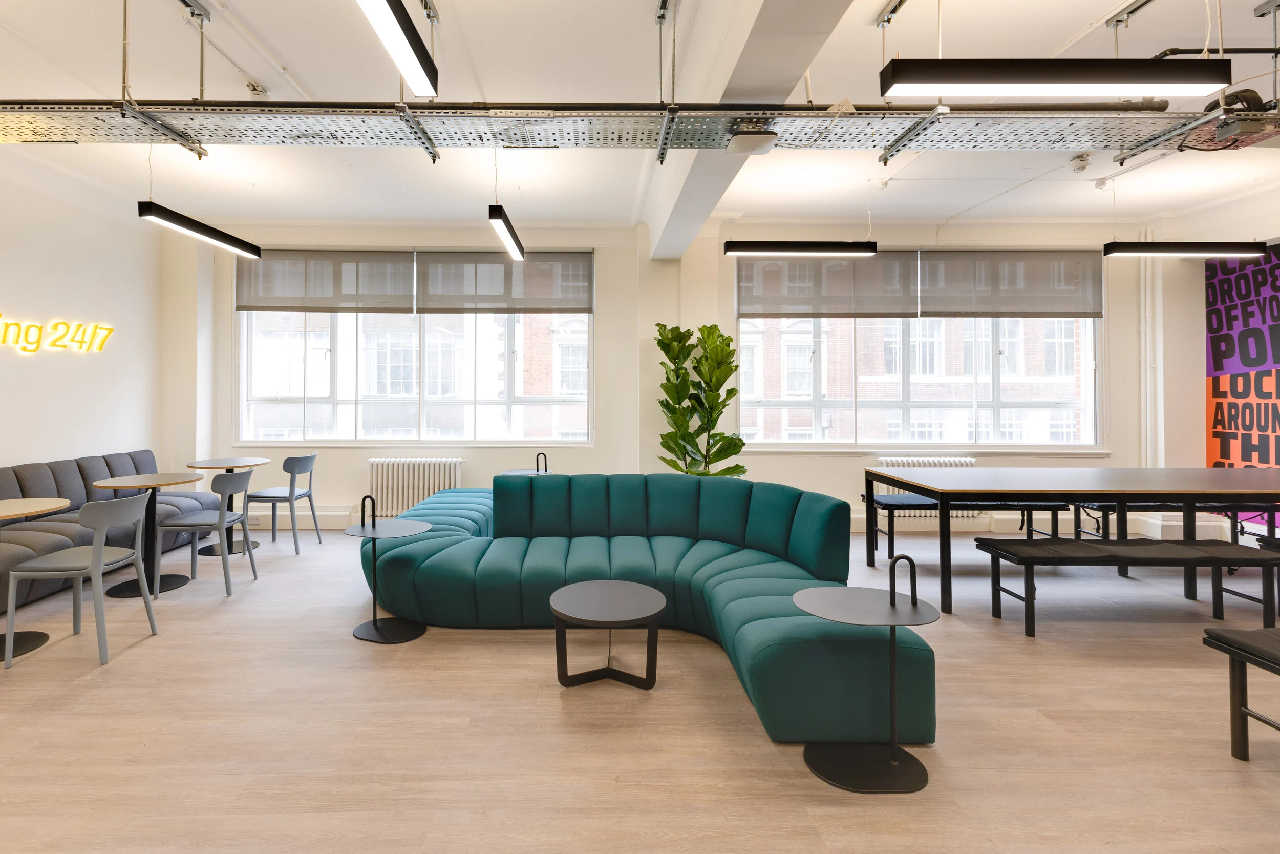 InPost office breakout space with curved teal seating, grey chairs, black tables, and large windows bringing in natural light.