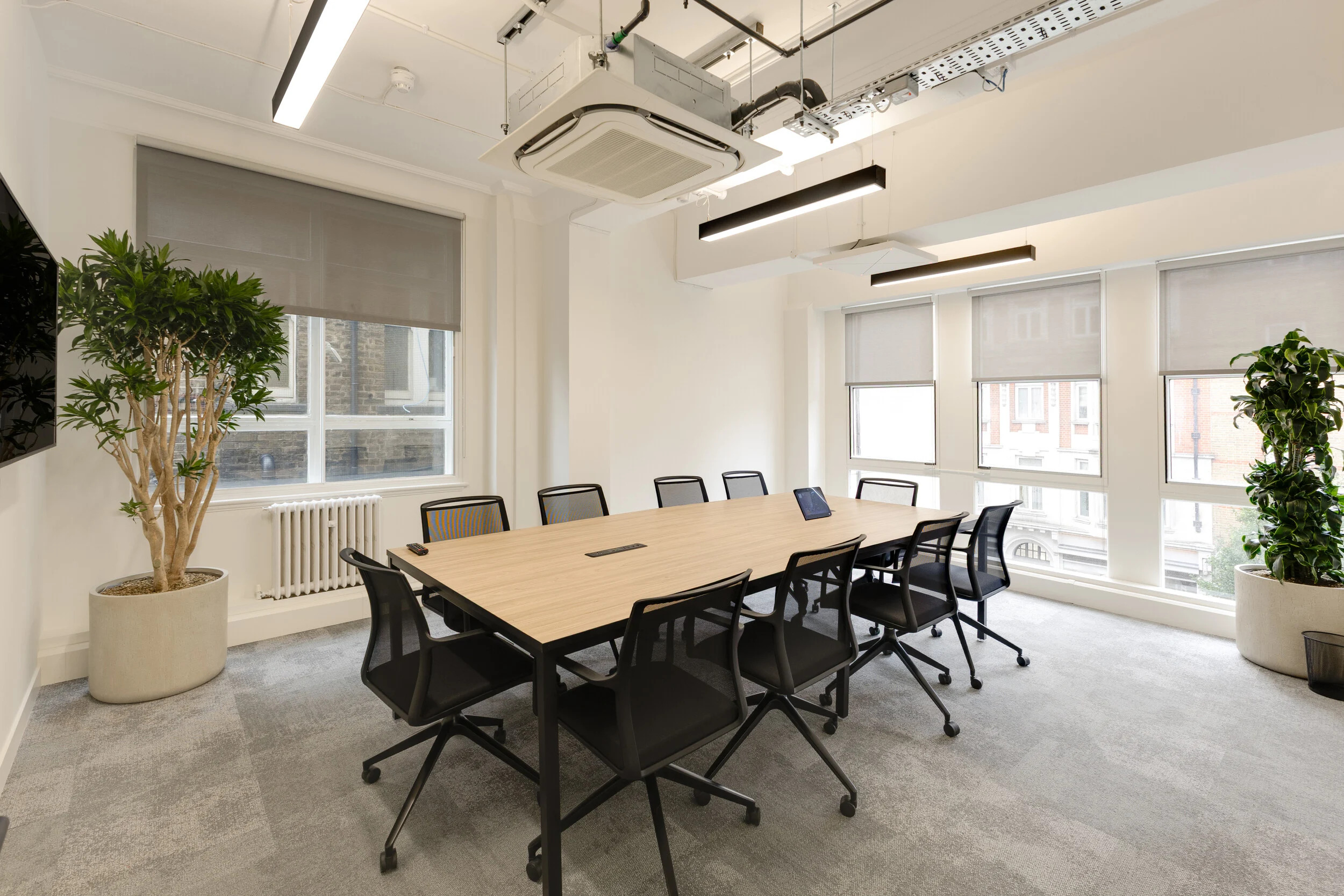 InPost office meeting room with a large wooden table, black mesh chairs, potted plants, and full-height windows bringing in natural light.