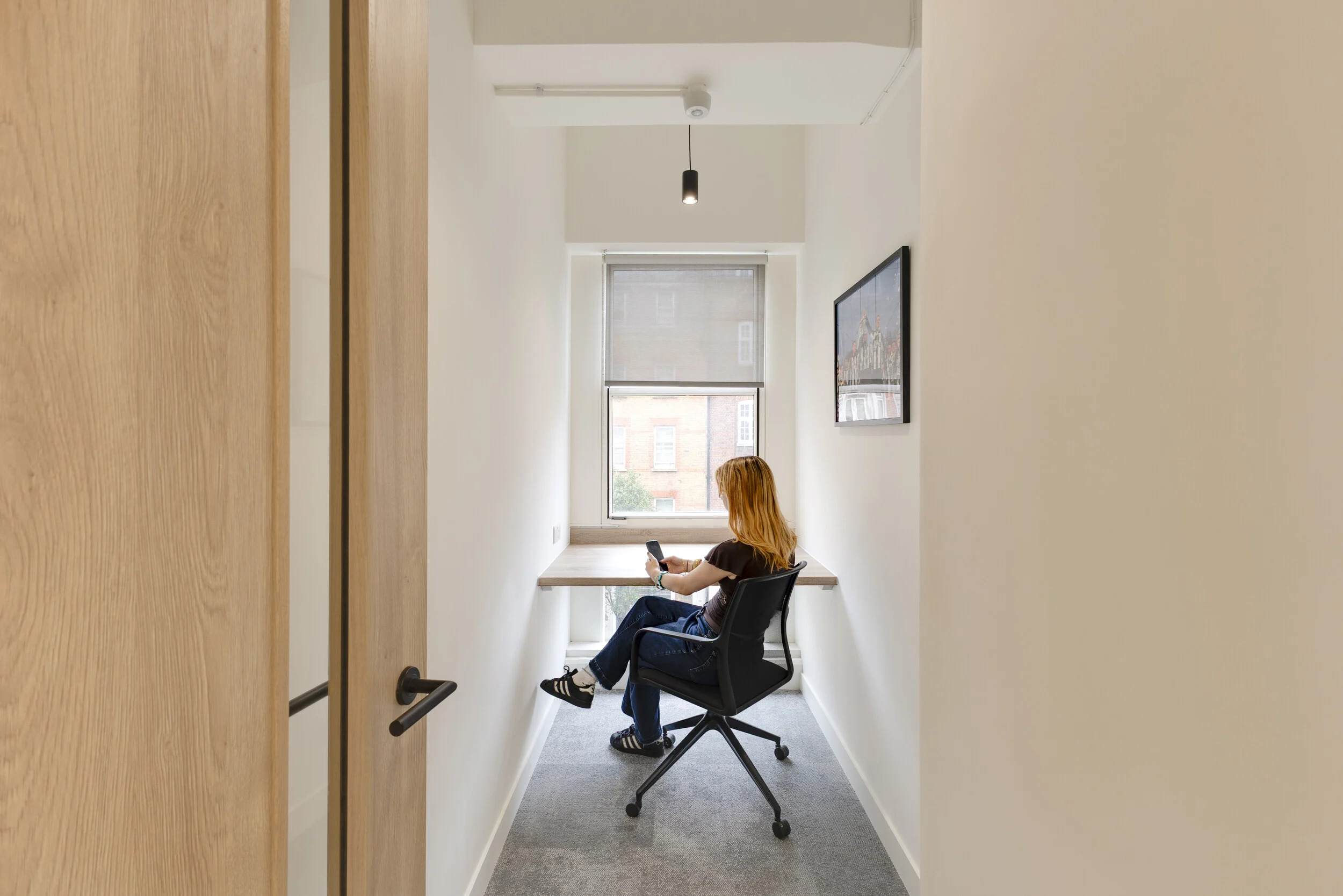 InPost office focus room with a single desk, ergonomic chair, large window, and an employee working on a phone.