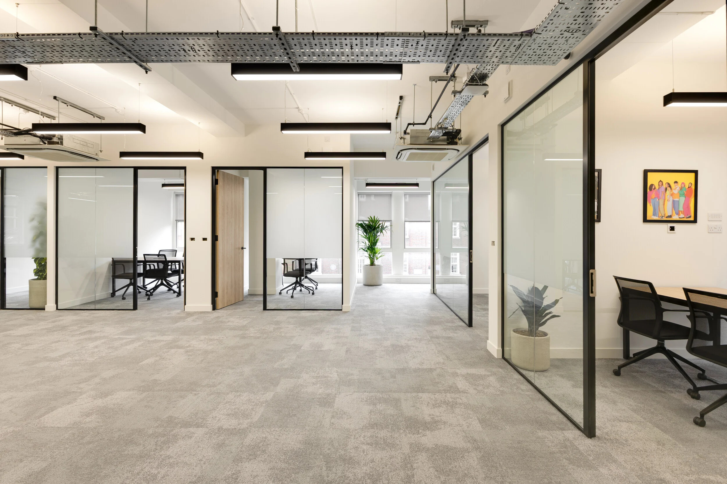 InPost office area with glass-fronted meeting rooms, grey carpet flooring, modern black chairs, potted plants, and exposed ceiling details.