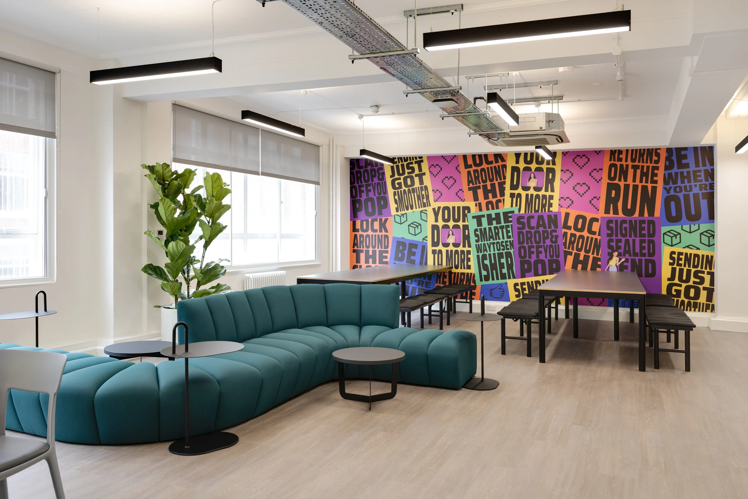 InPost breakout area by WFG with curved teal seating, black tables and benches, large potted plant, and a colourful branded wall mural with bold typography.