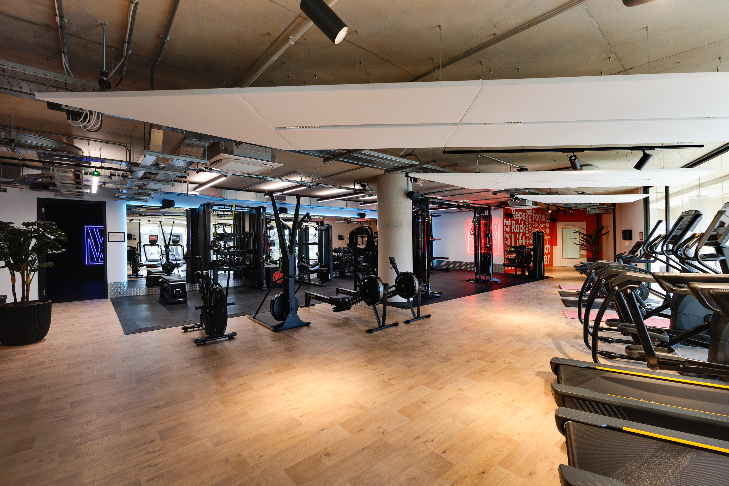Wide view of the reFIT The Welcome Building gym showcasing treadmills, rowing machines, and strength training areas with modern lighting and bold neon accents.