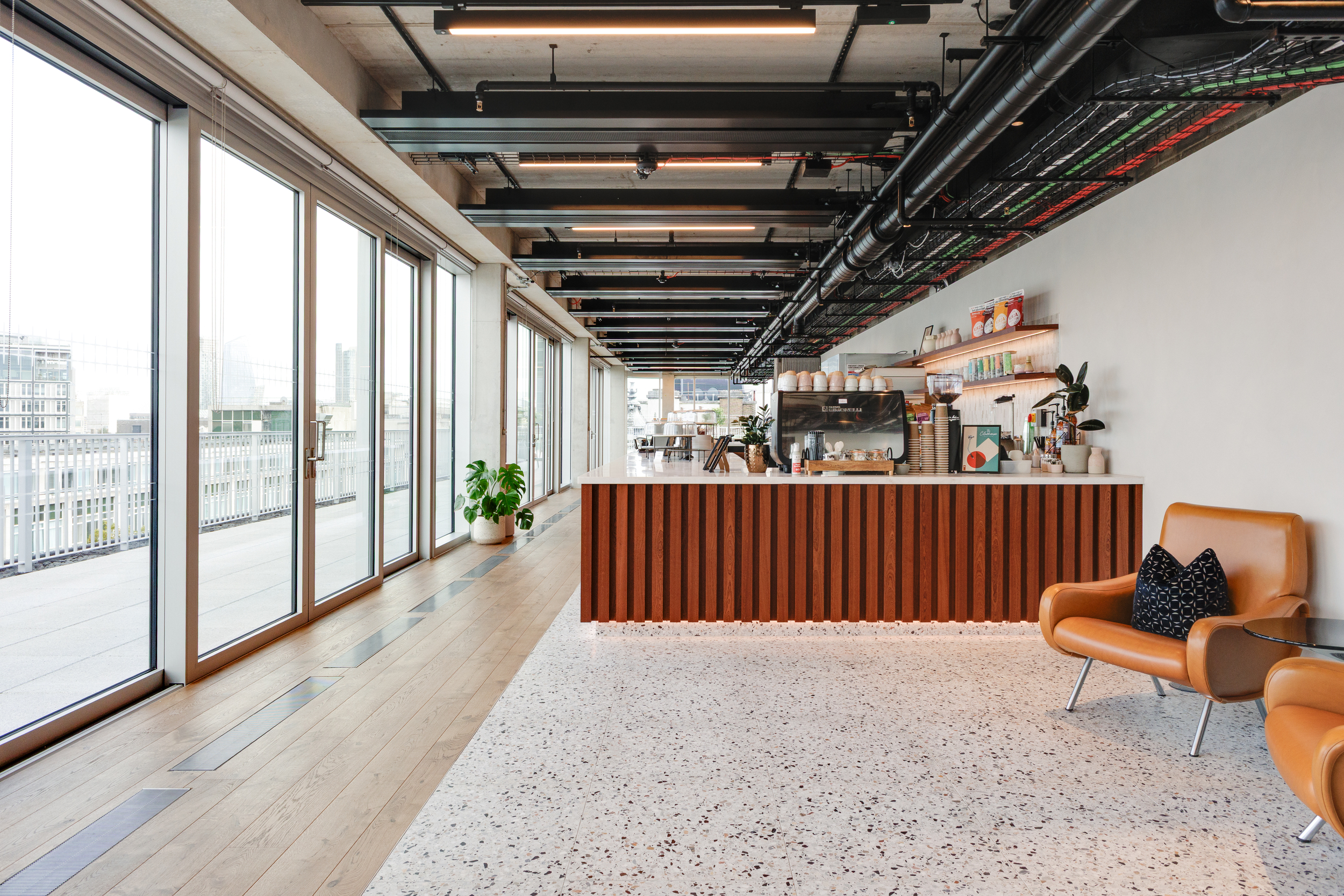 Café-style bar at the Space House Clubhouse with terrazzo flooring, walnut finishes, and tan leather seating, showcasing Modus and Platfform’s hospitality-led workplace concept.