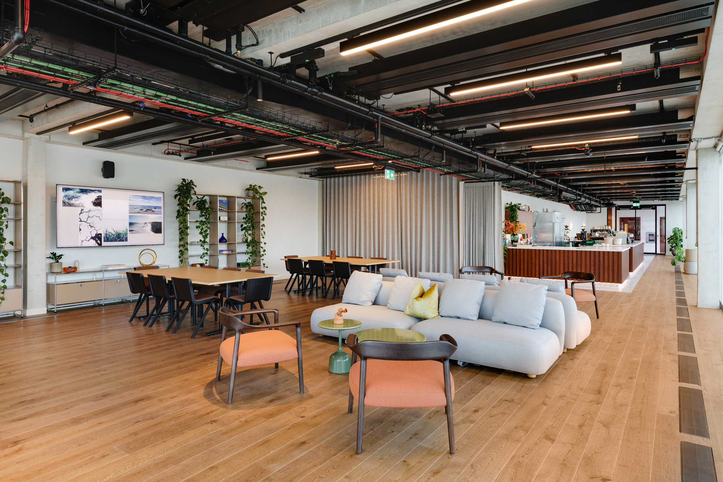 Open-plan interior of the Space House Clubhouse with lounge seating, dining tables, and a walnut bar, showcasing Modus and Platfform’s balance of Brutalist structure and warm, flexible furnishings.