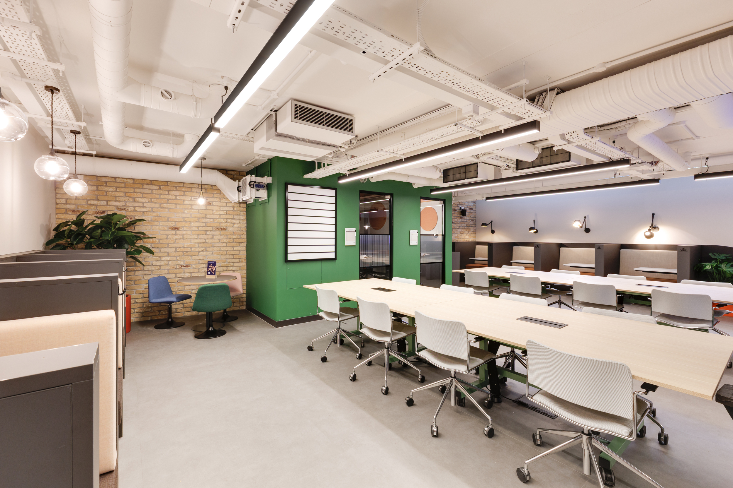 Coworking area at Work.Life Clerkenwell Green with green walls, exposed brickwork and shared tables with pale chairs, blending industrial character with modern design from Two and Platfform.