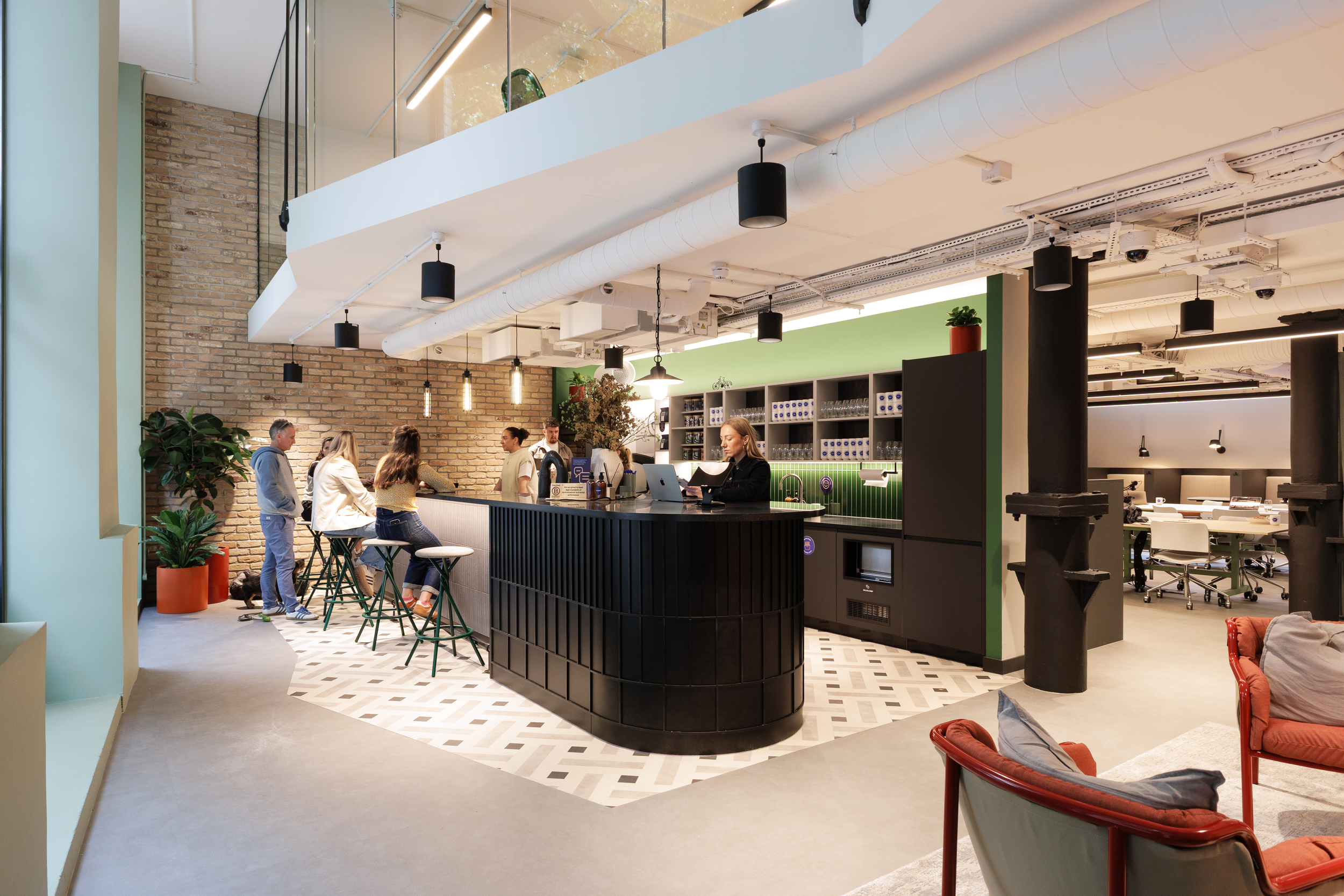 Ground floor café and workspace at Work.Life Clerkenwell Green with a black counter, green tiled wall and exposed brick backdrop, reflecting the collaborative design approach of Two and Platfform.