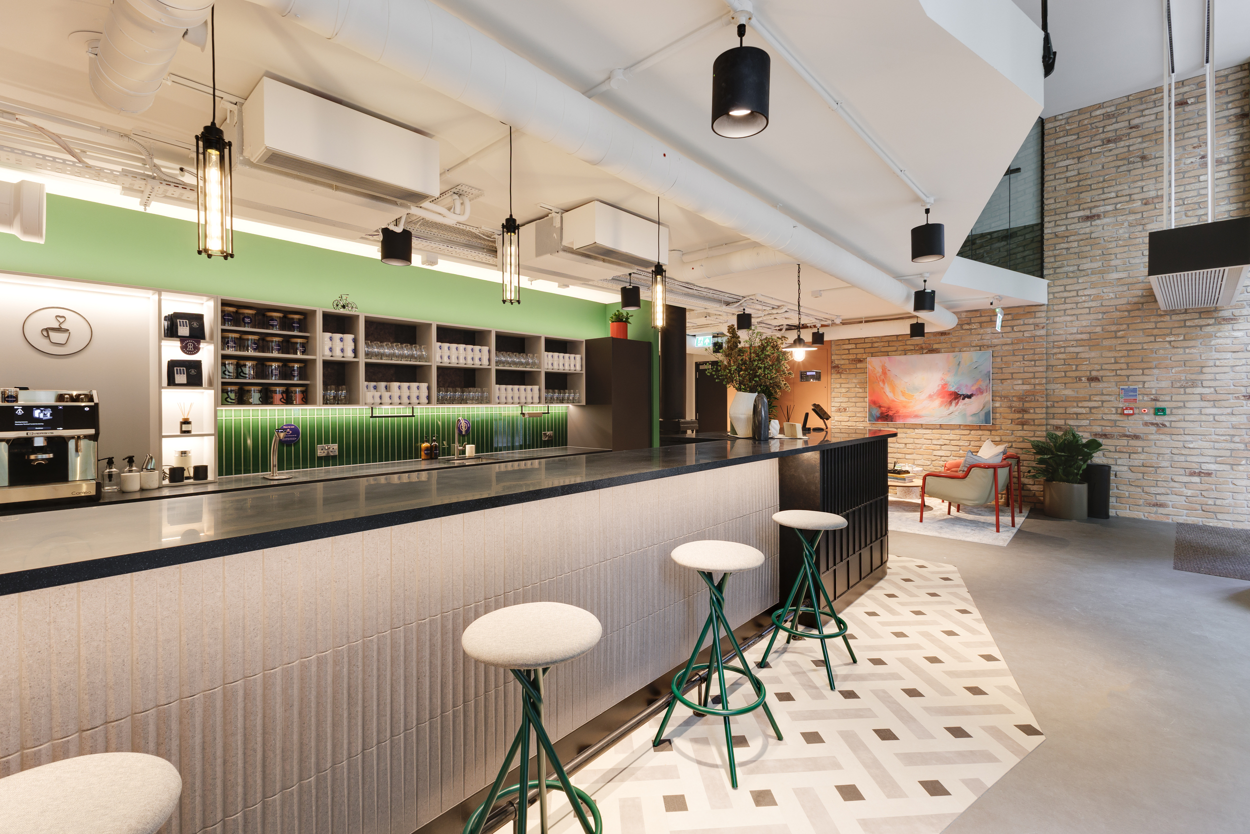 Ground floor teapoint at Work.Life Clerkenwell Green with a tiled counter, green splashback and bar seating, leading into a lounge area, furnished through Two and Platfform.