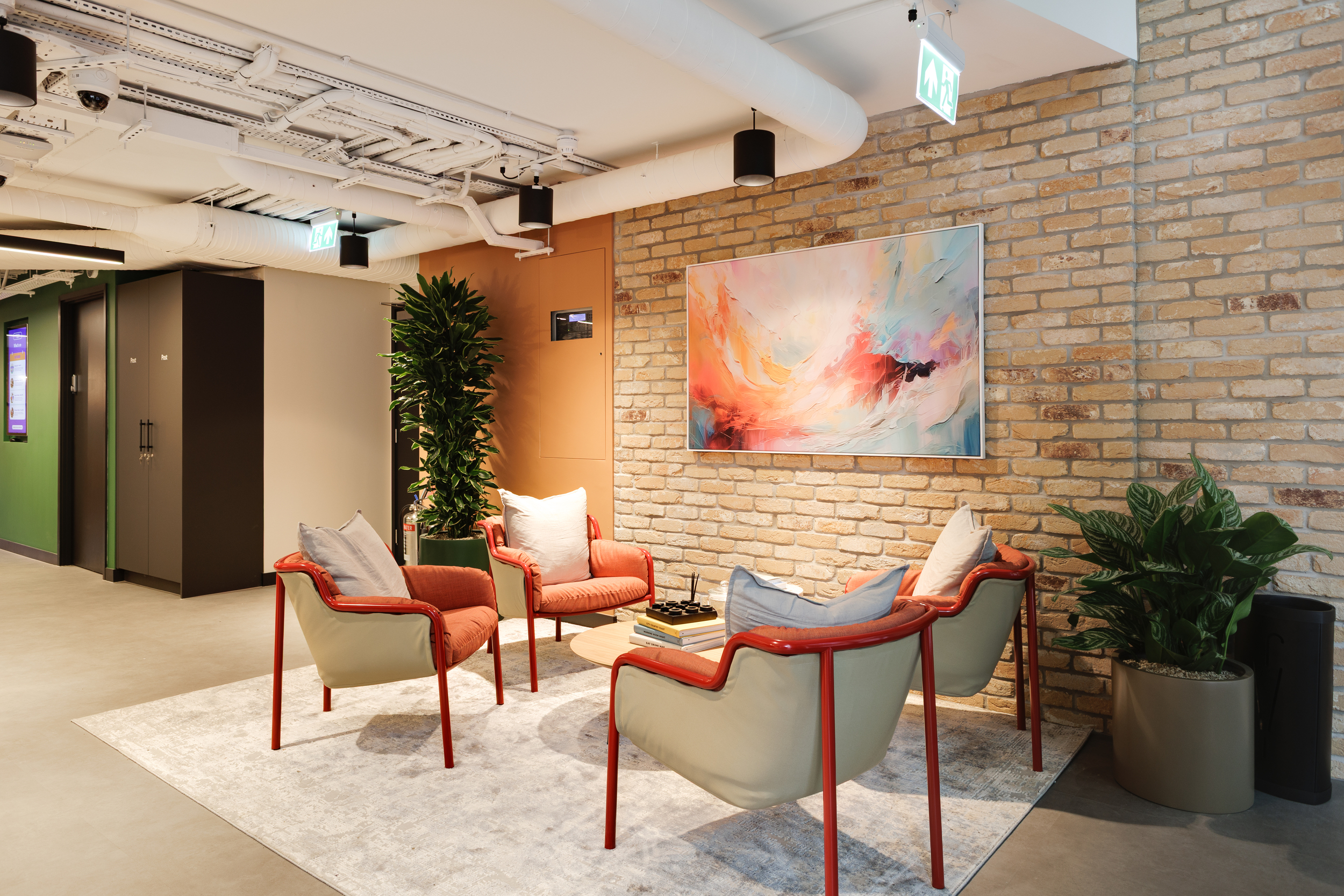 Lounge seating area at Work.Life Clerkenwell Green with red-framed armchairs, a colourful abstract artwork and exposed brick walls, furnished through Two and Platfform.